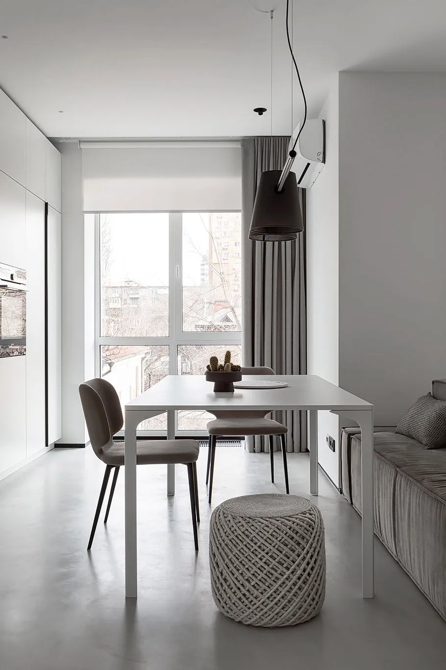 A modern minimalist living and dining room with a sleek white table and chairs, a large window, and a comfortable sofa.