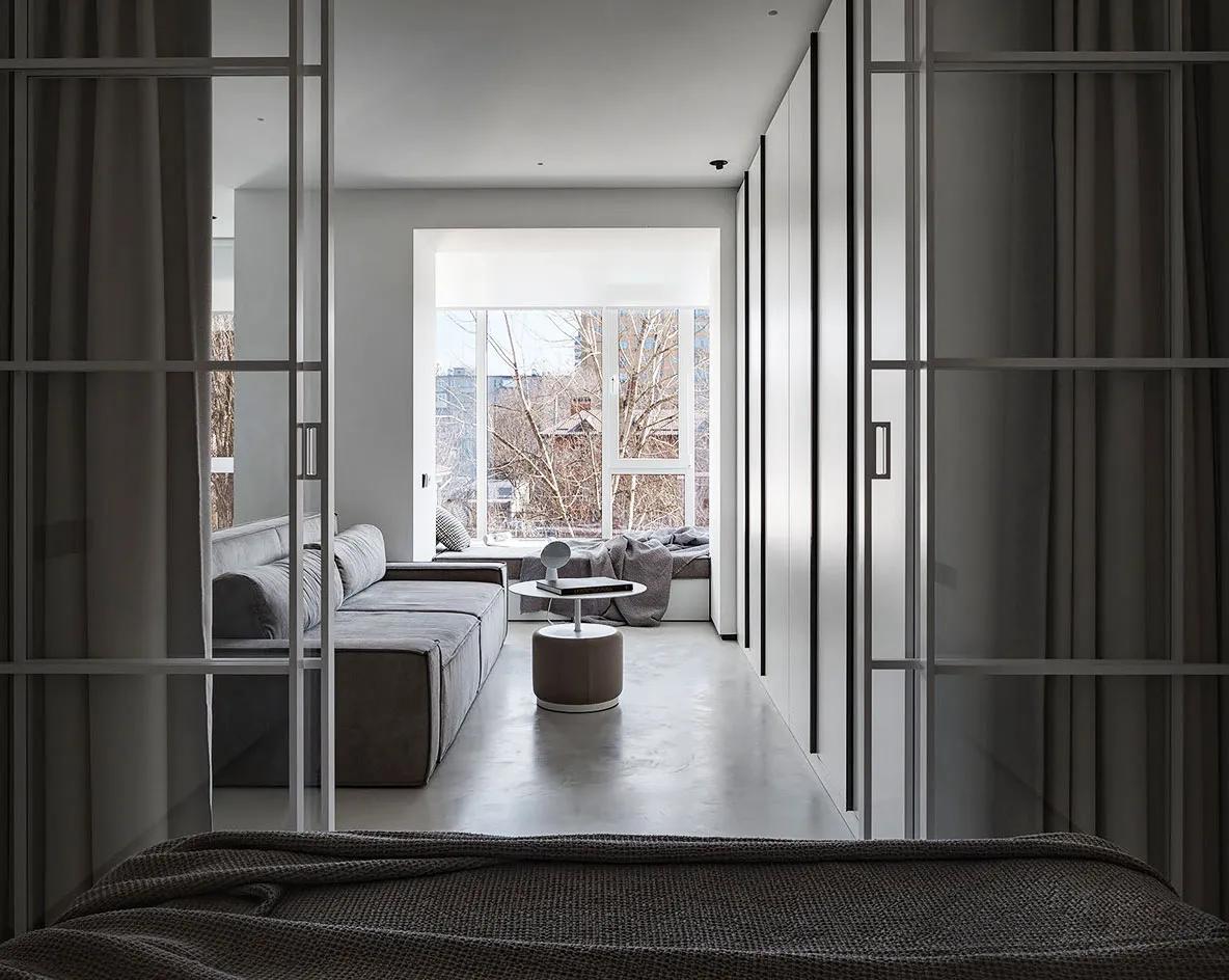 A modern living room featuring a concrete sectional sofa and a circular ottoman with a book on top.