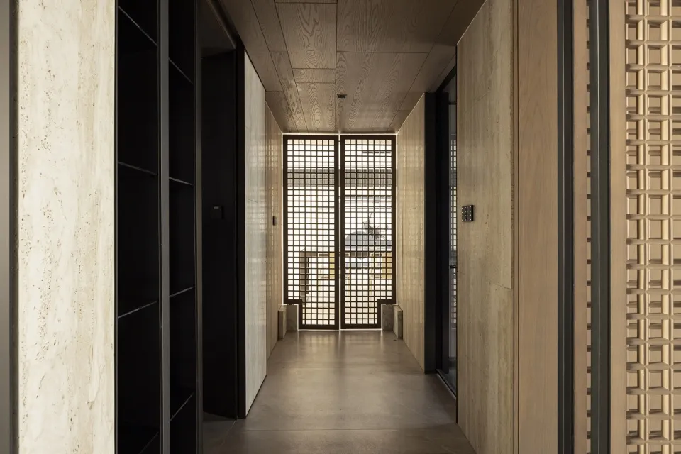 A minimalist corridor with wooden walls and a wooden ceiling, featuring a grid-patterned glass door.