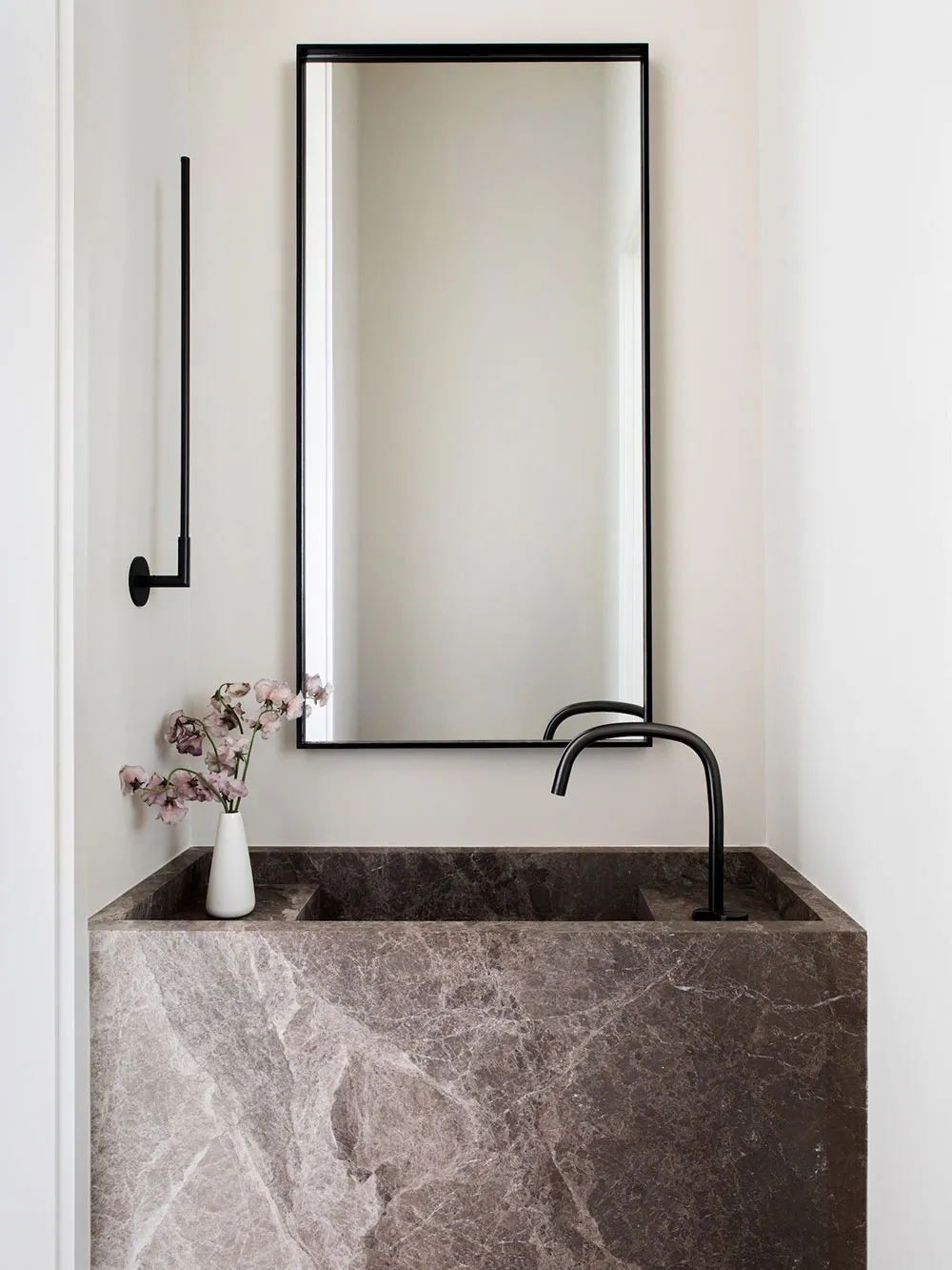 A modern minimalist bathroom featuring a marble sink, black faucet, and a vase of flowers on the counter.