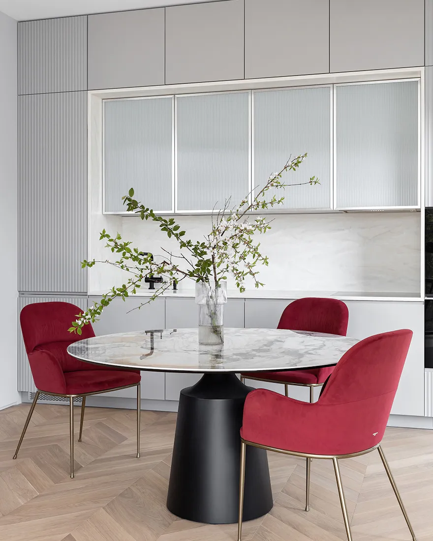 A modern dining room with a round marble table and red upholstered chairs.