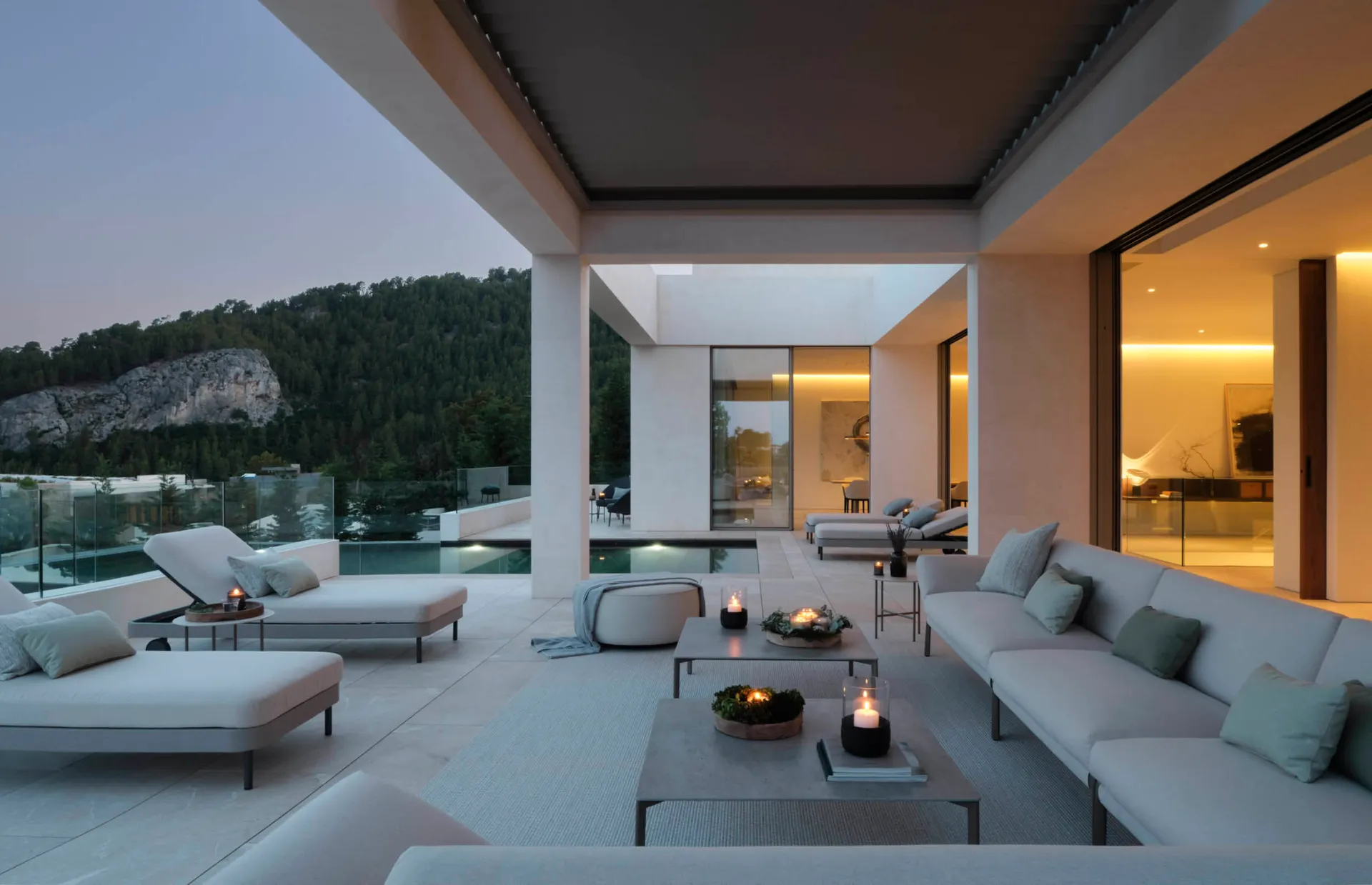 A modern outdoor living space featuring concrete flooring and furniture, with a view of mountains and trees.