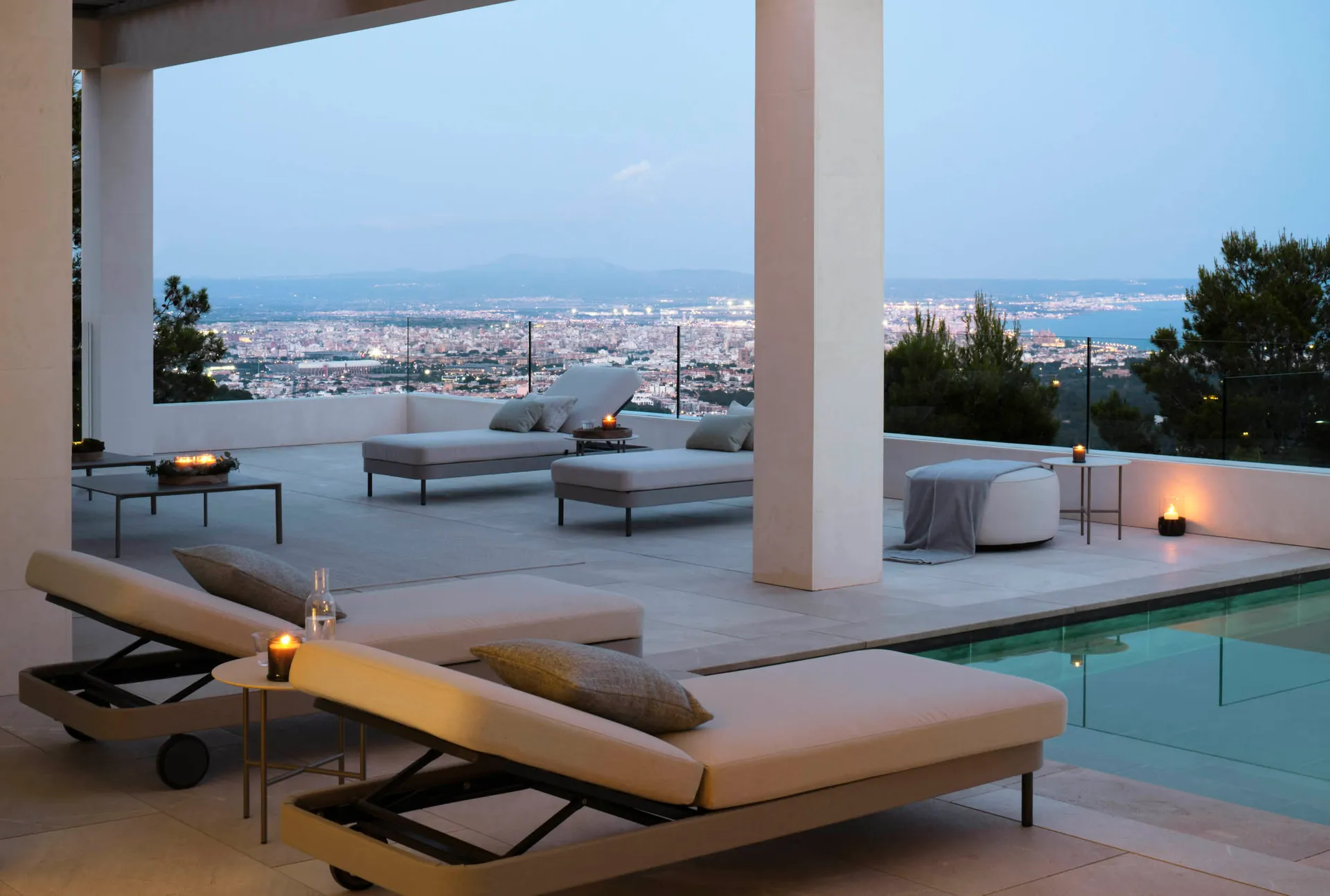 A modern pool deck with concrete seating areas overlooking a cityscape at dusk.