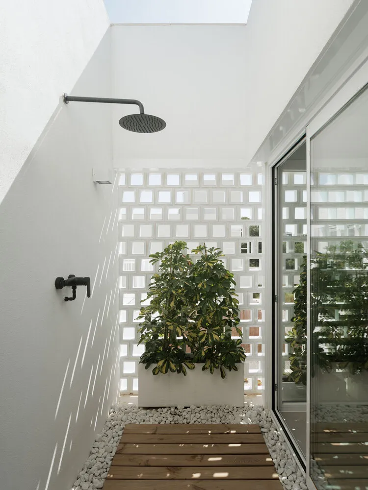 An outdoor shower with minimalist design, featuring concrete walls and a wooden platform surrounded by white rocks, with a la
