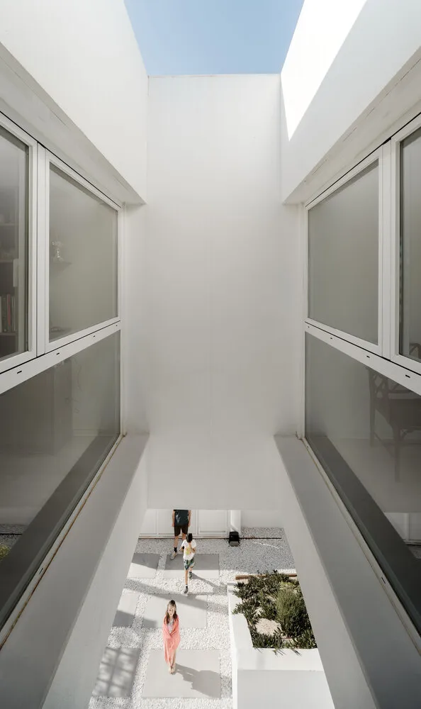 A modern house with a minimalist design featuring a central courtyard made of white concrete tiles, surrounded by clear glass