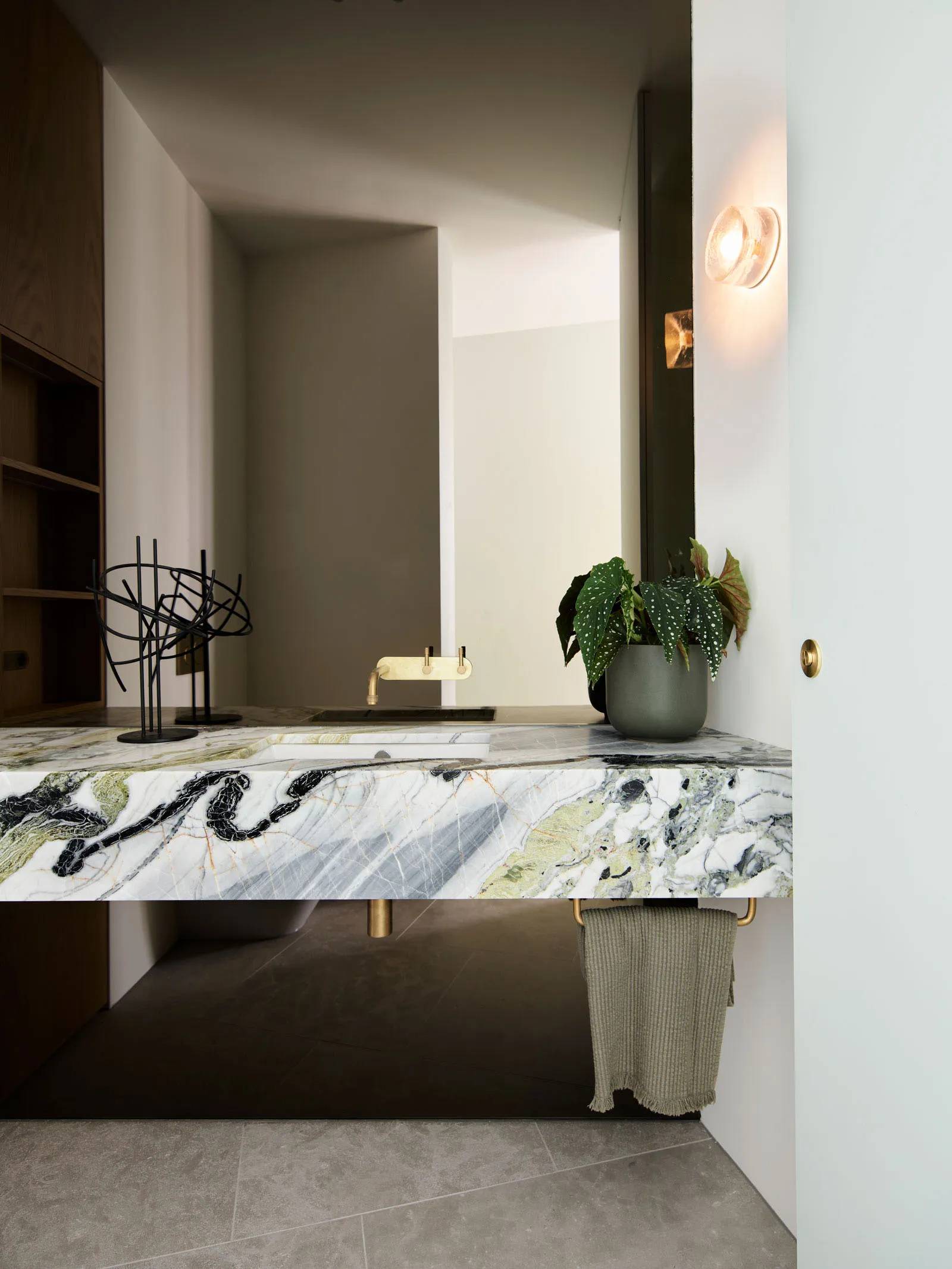 現代衛浴空間,配有大理石檯面、黃銅水龍頭與綠色植栽。