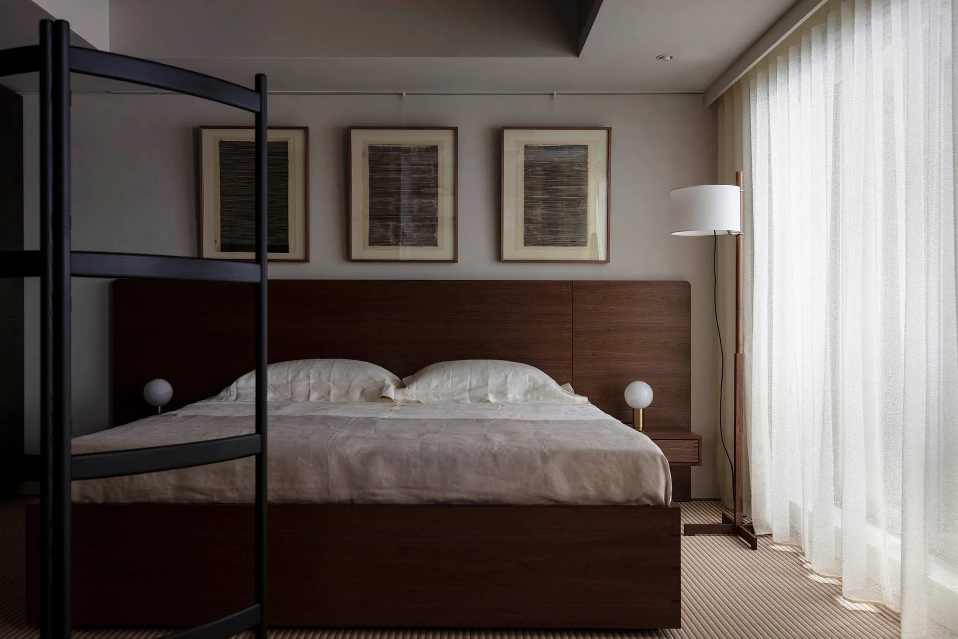 A minimalist bedroom with a wooden bed frame and a window with sheer curtains.