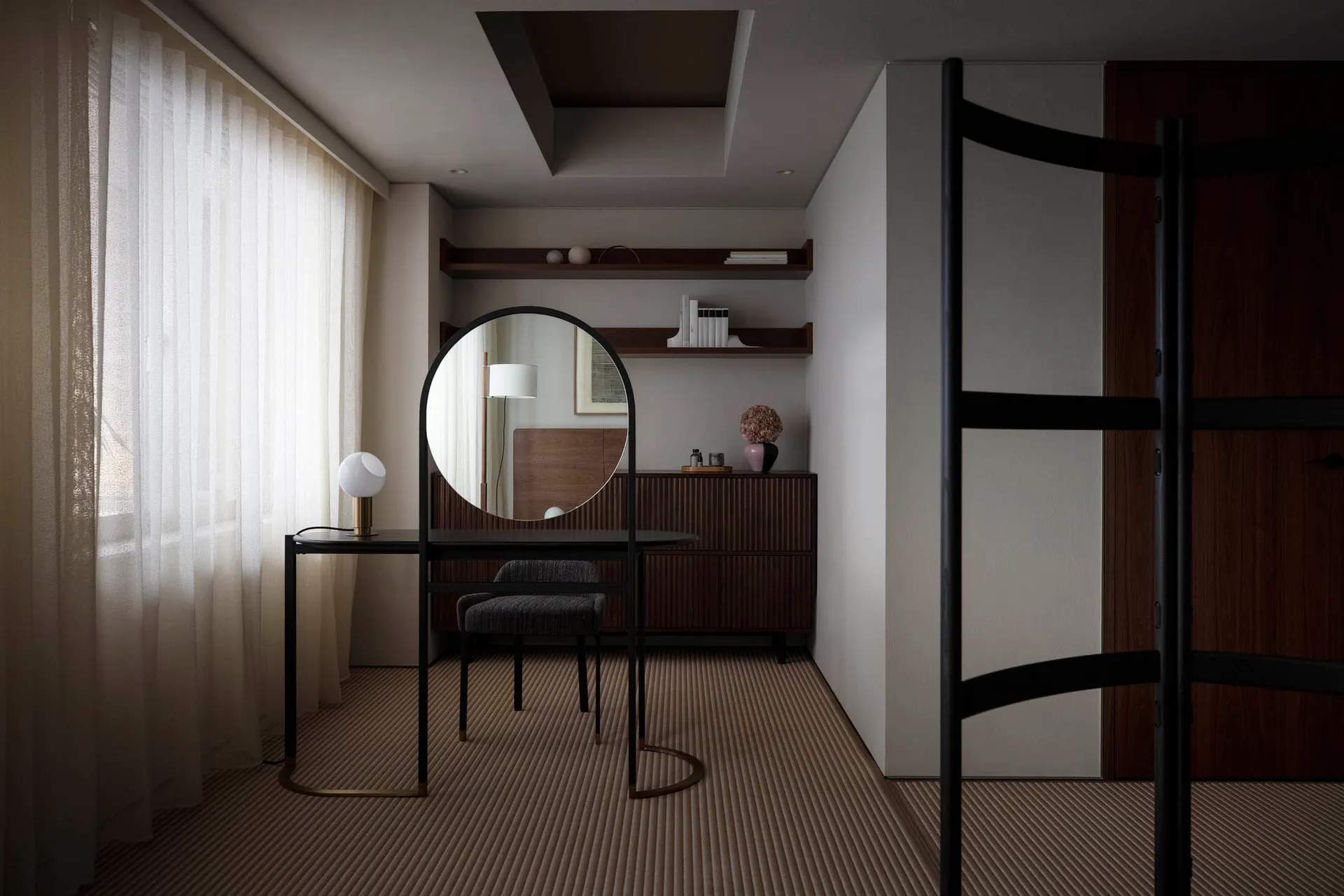 Modern minimalist interior featuring a metal-framed round mirror standing on a black desk with a small round table lamp on it