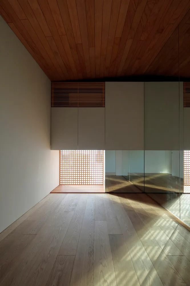 Minimalist design interior with wooden flooring and light filtering through a lattice window.