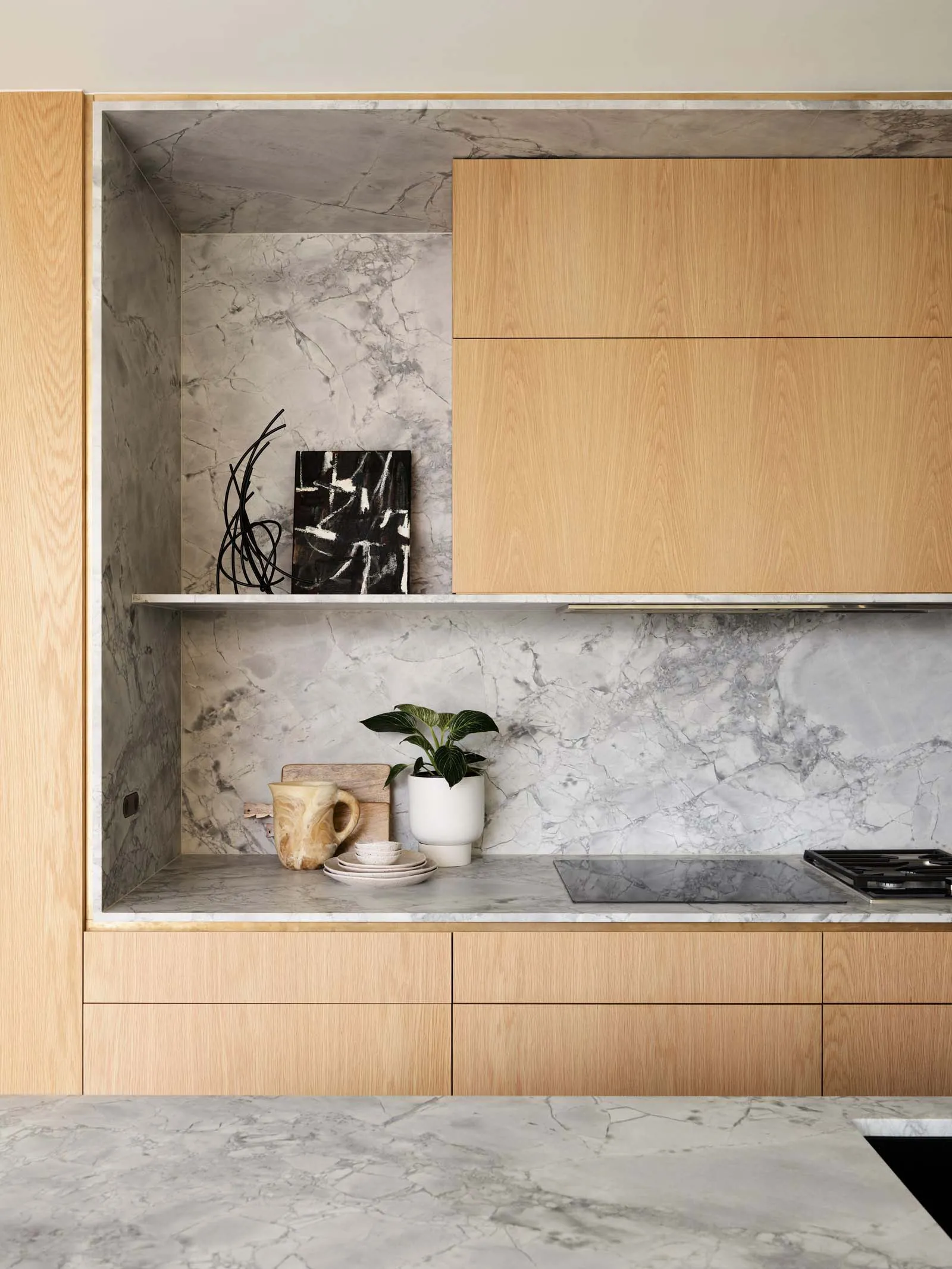 A minimalist residential kitchen featuring marble finishes and wooden cabinets.