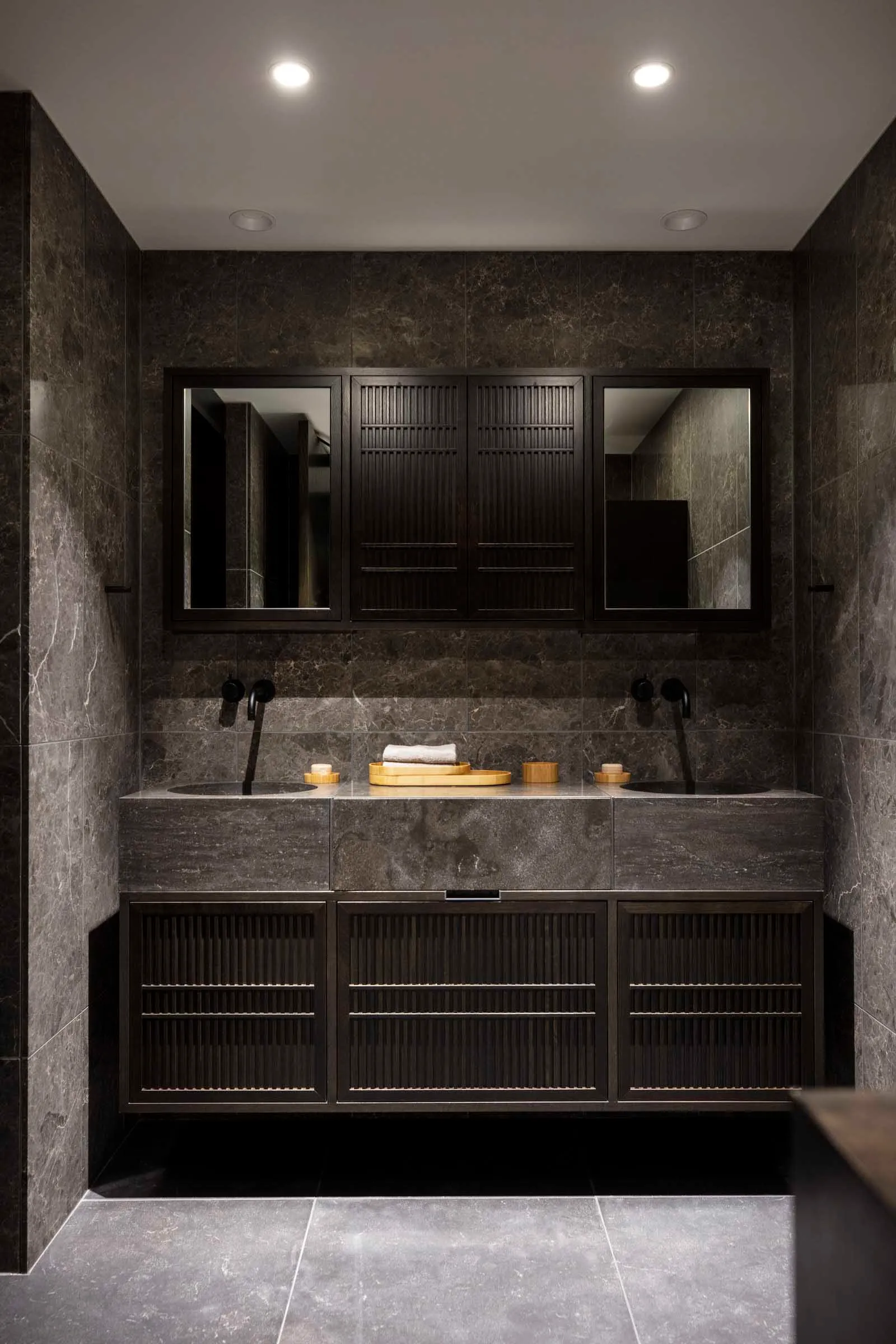 A modern bathroom with black marble tiles and a double vanity sink.