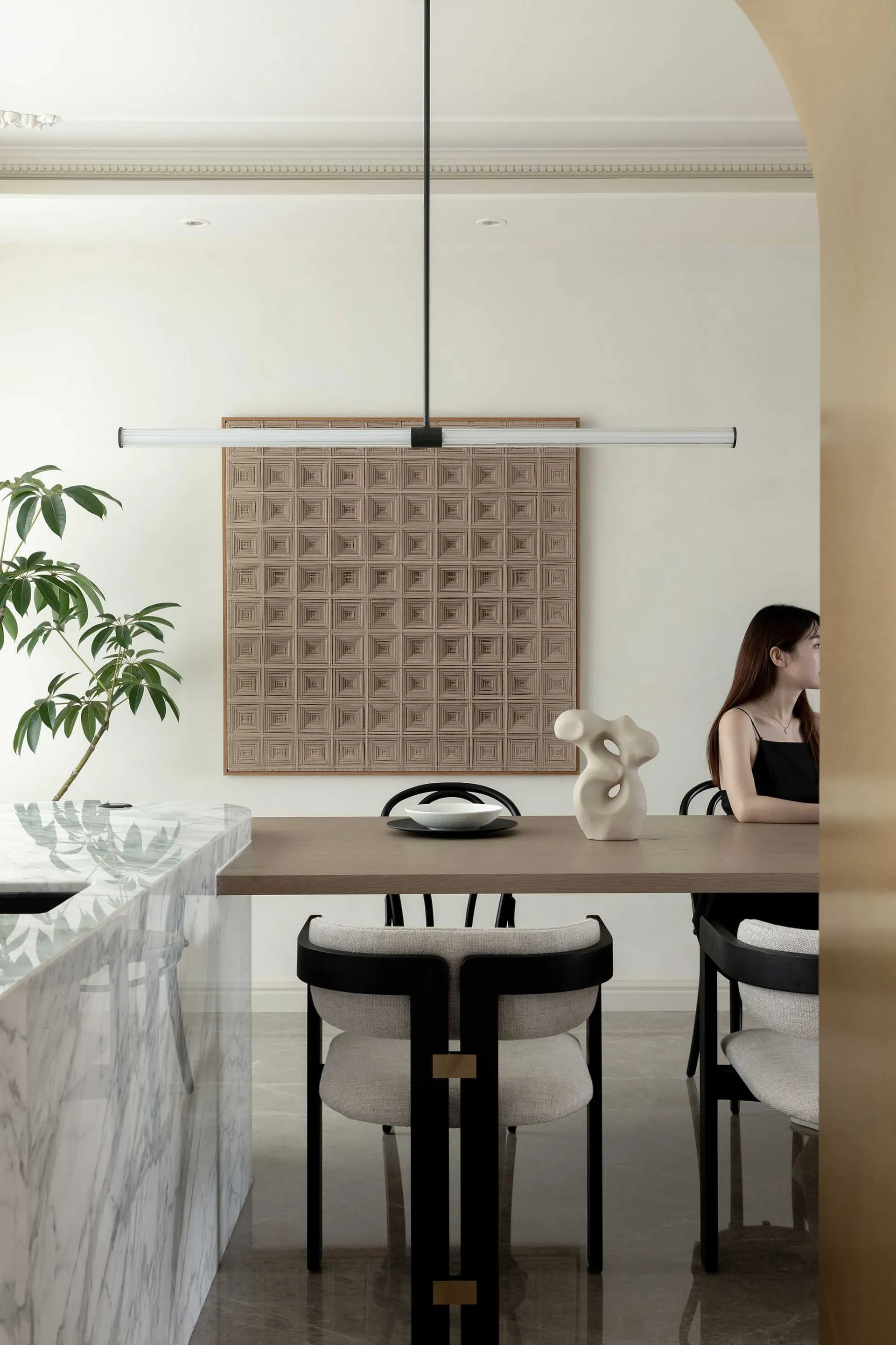 A modern dining room featuring a marble and wood table with leather upholstered chairs, a minimalist sculpture, and a pattern