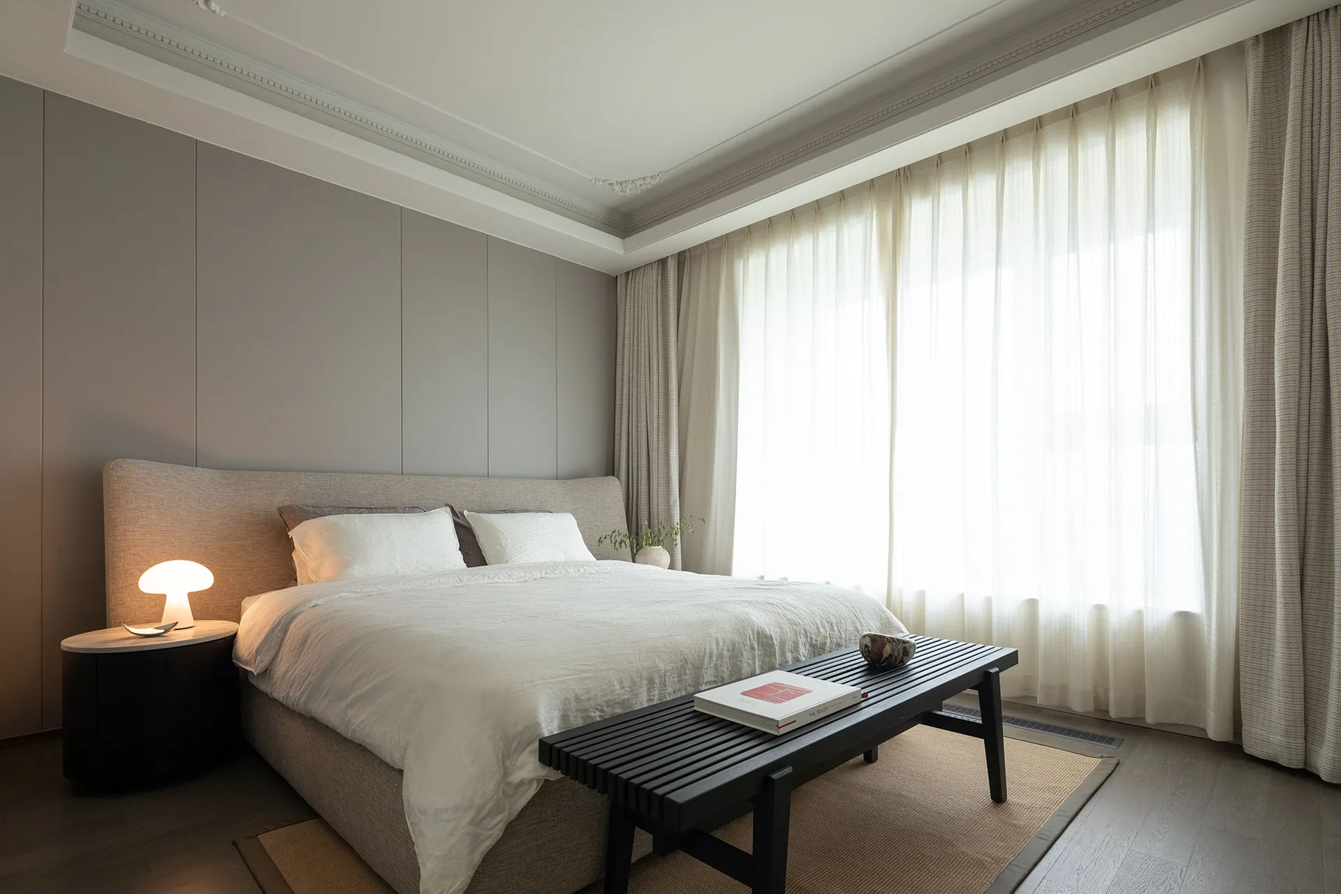 A minimalist bedroom designed with gray and taupe tones, featuring a large bed with soft bedding, a side table with a table l