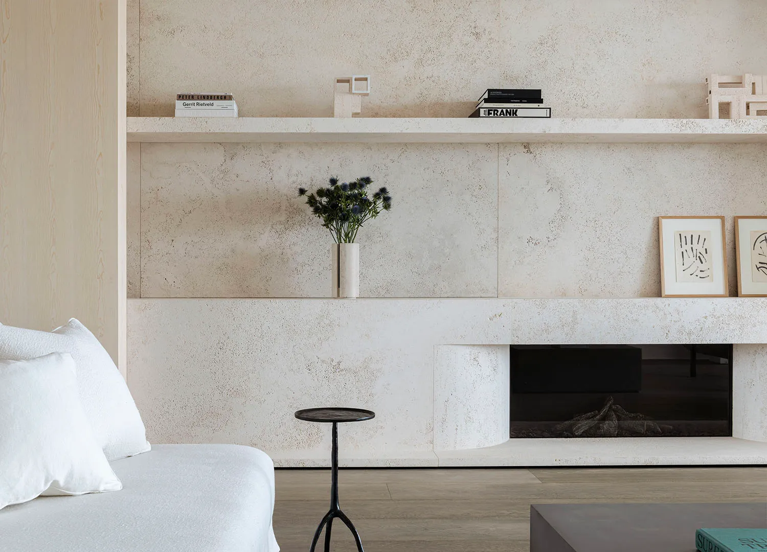 A minimalist living room with a concrete wall, white furniture, and a black metal side table.