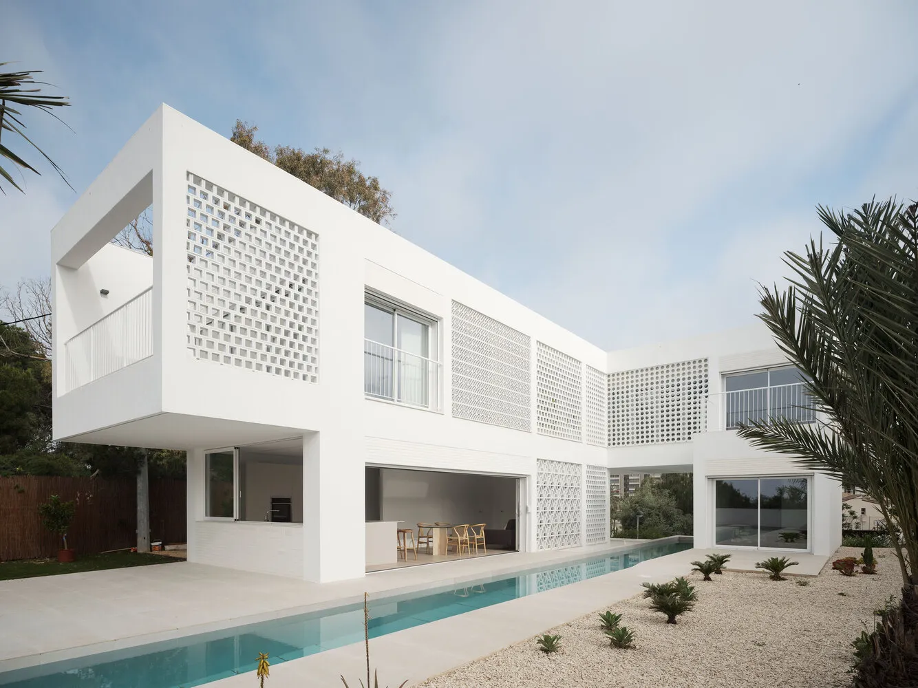 A minimalist modern house with a white concrete exterior, featuring a balcony and a swimming pool.