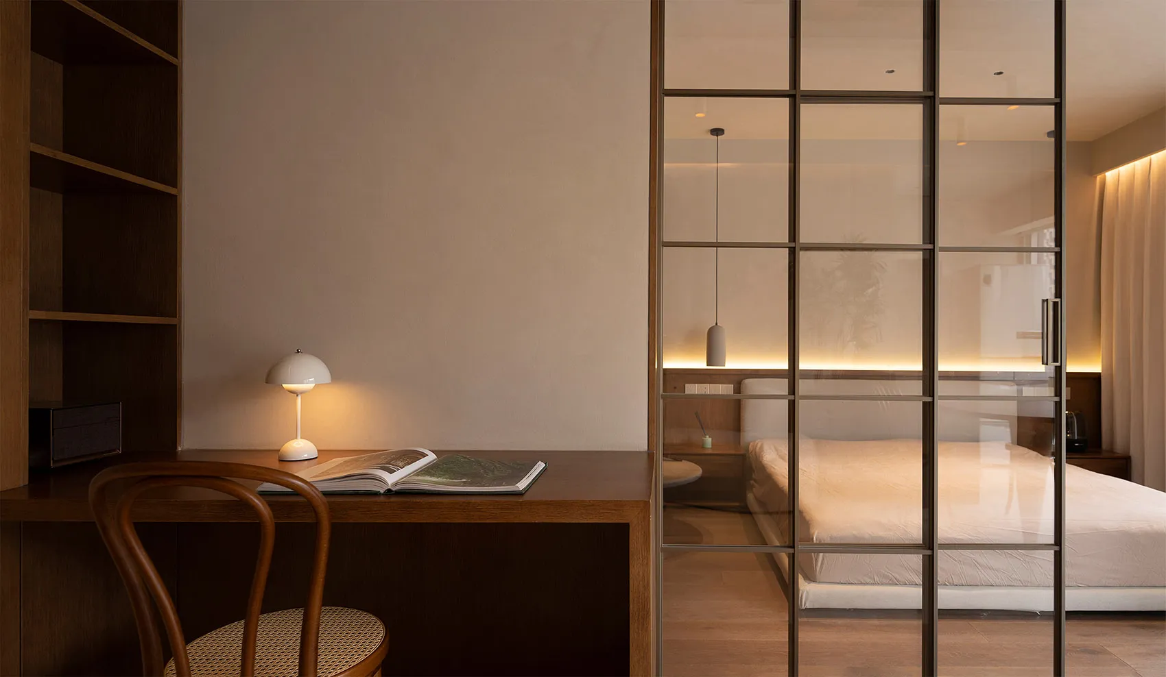A minimalist bedroom featuring a wooden desk with a table lamp and an open book.