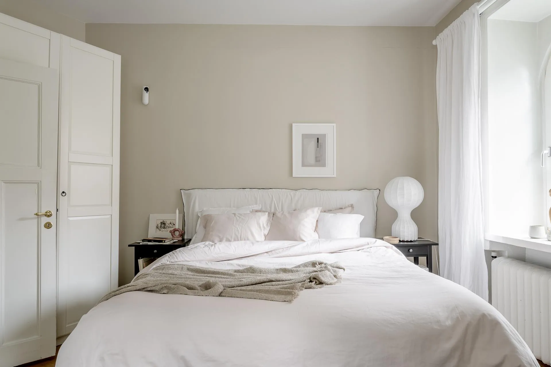 A minimalist bedroom featuring a white bed, white walls, and a white headboard.