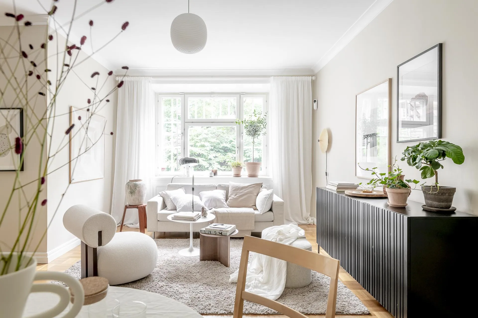 A modern minimalist living room featuring a white sofa, wooden coffee table, and floor-to-ceiling windows with white curtains