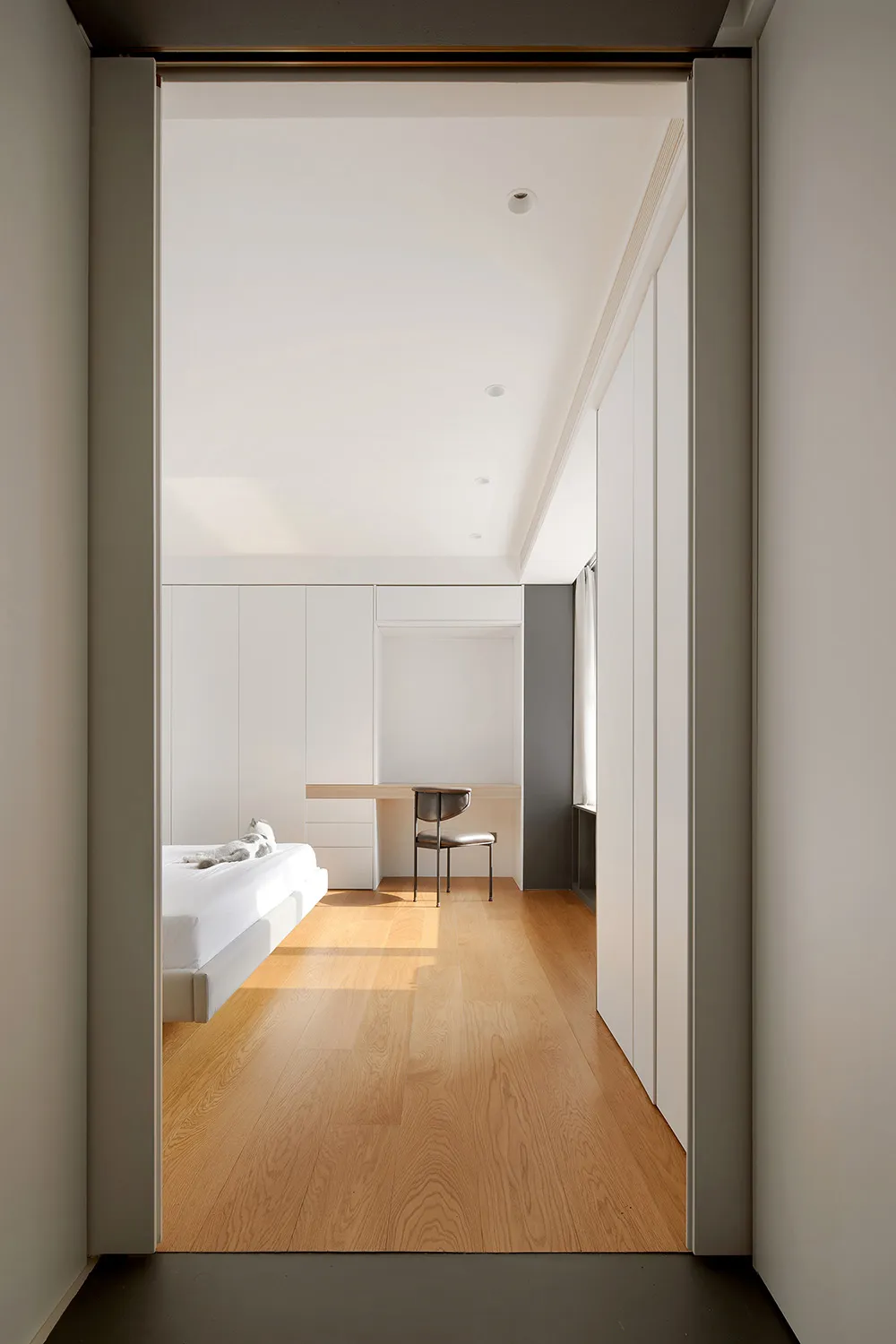 A minimalist bedroom with white walls, a wooden floor, and furniture.
