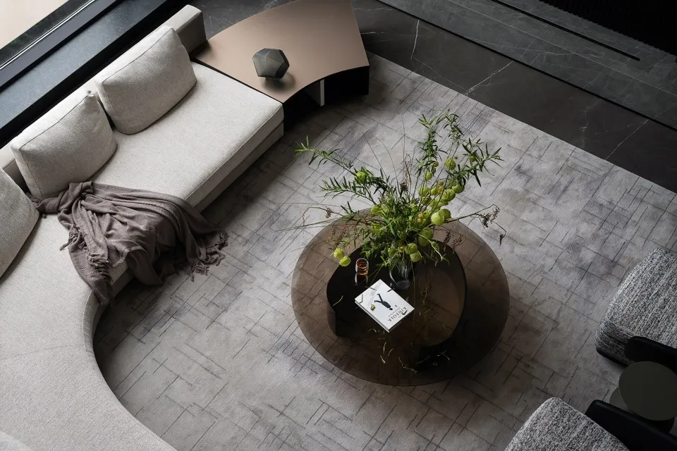 A minimalist living room featuring a fabric sectional sofa, a round coffee table with a vase of greenery, and a modern coffee