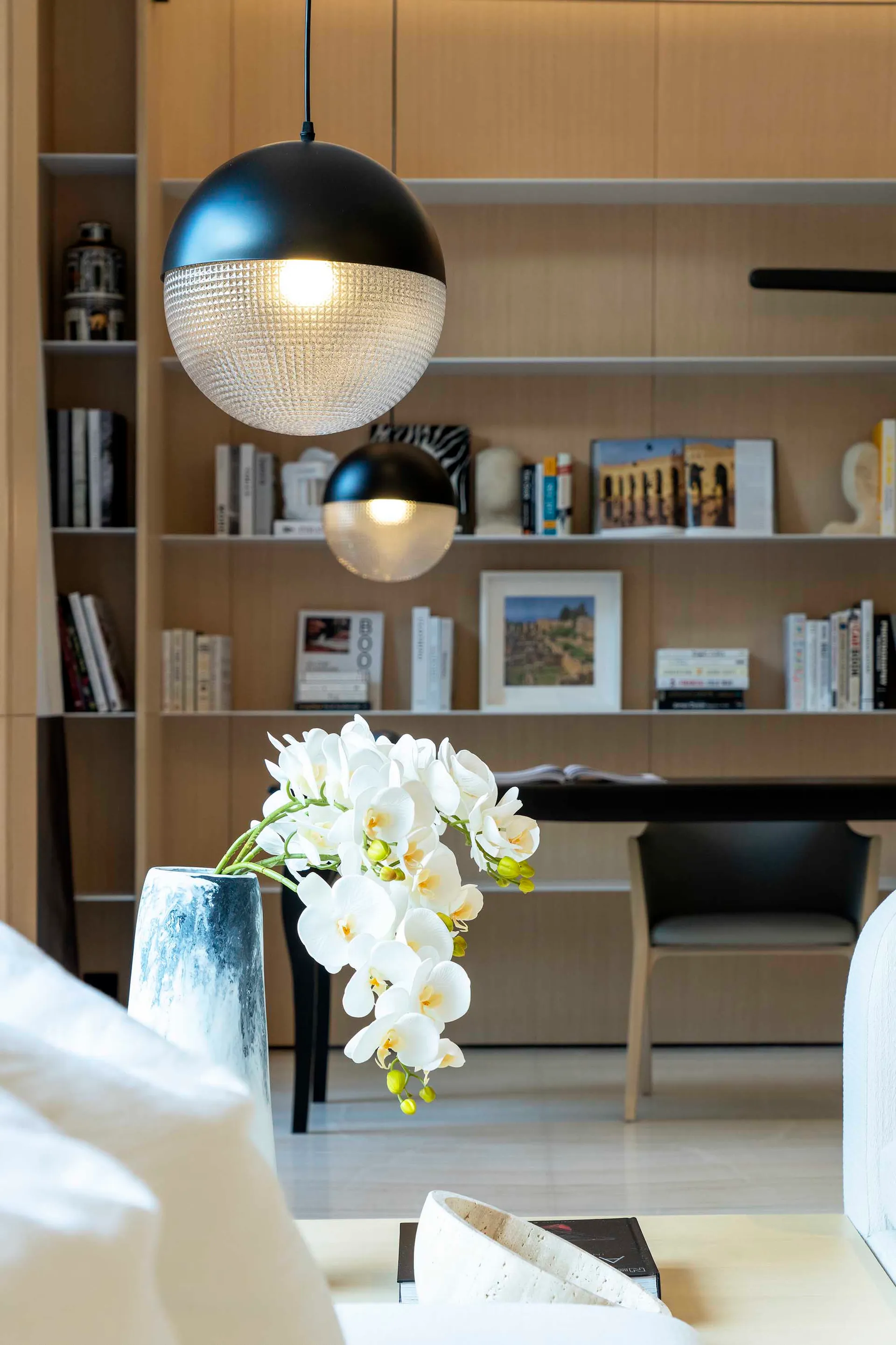 A minimalist living room featuring white floral arrangement on a wooden side table, with a wall-mounted bookshelf and black p