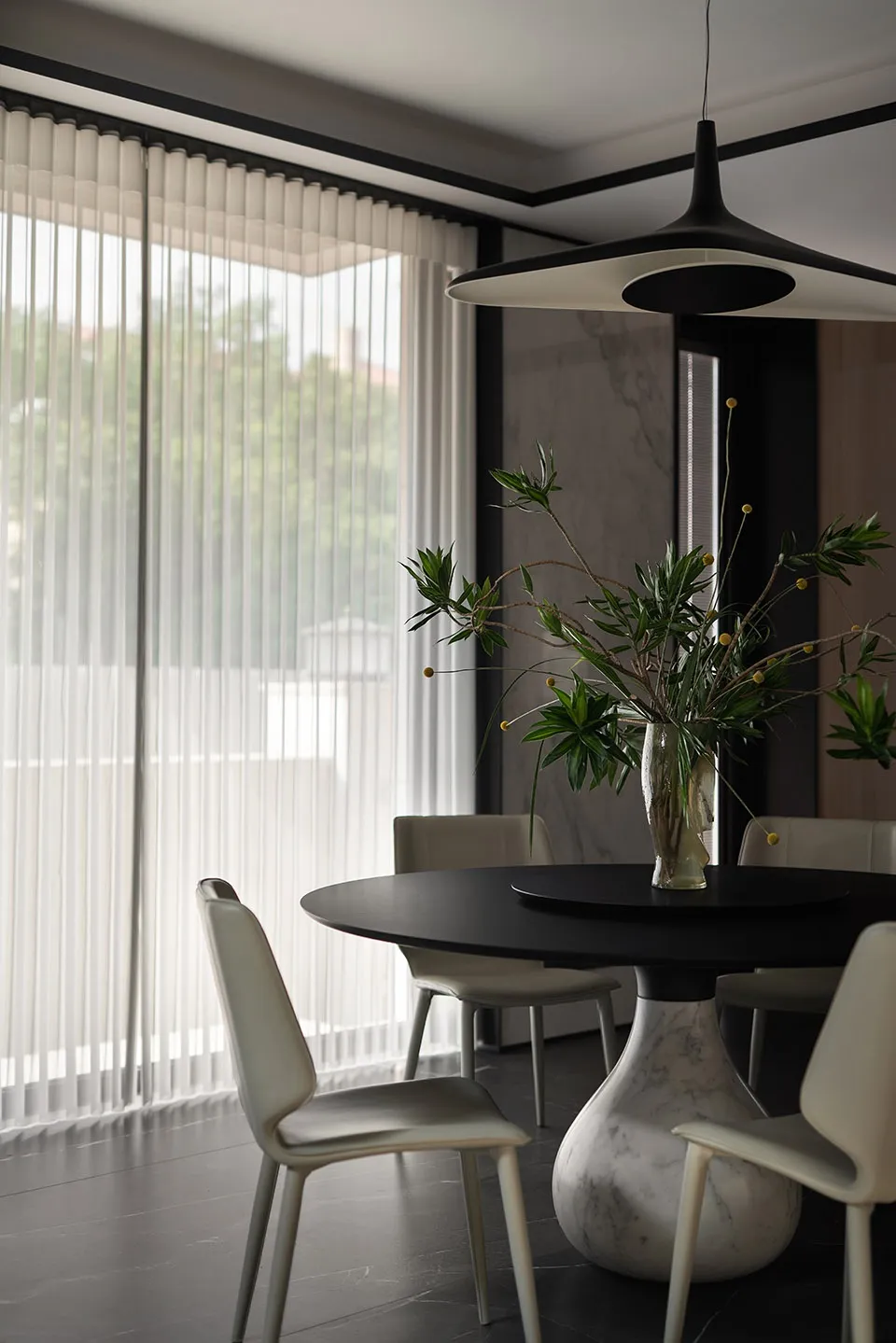A modern dining room featuring a round black marble table and sleek white chairs under a contemporary pendant light.