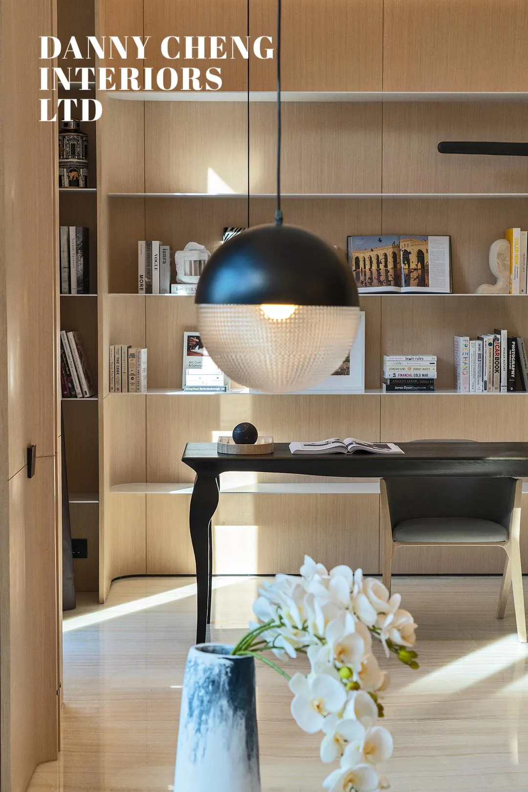 Modern home office featuring a wall of built-in bookshelves and wood furniture, with a pendant light fixture hanging above a