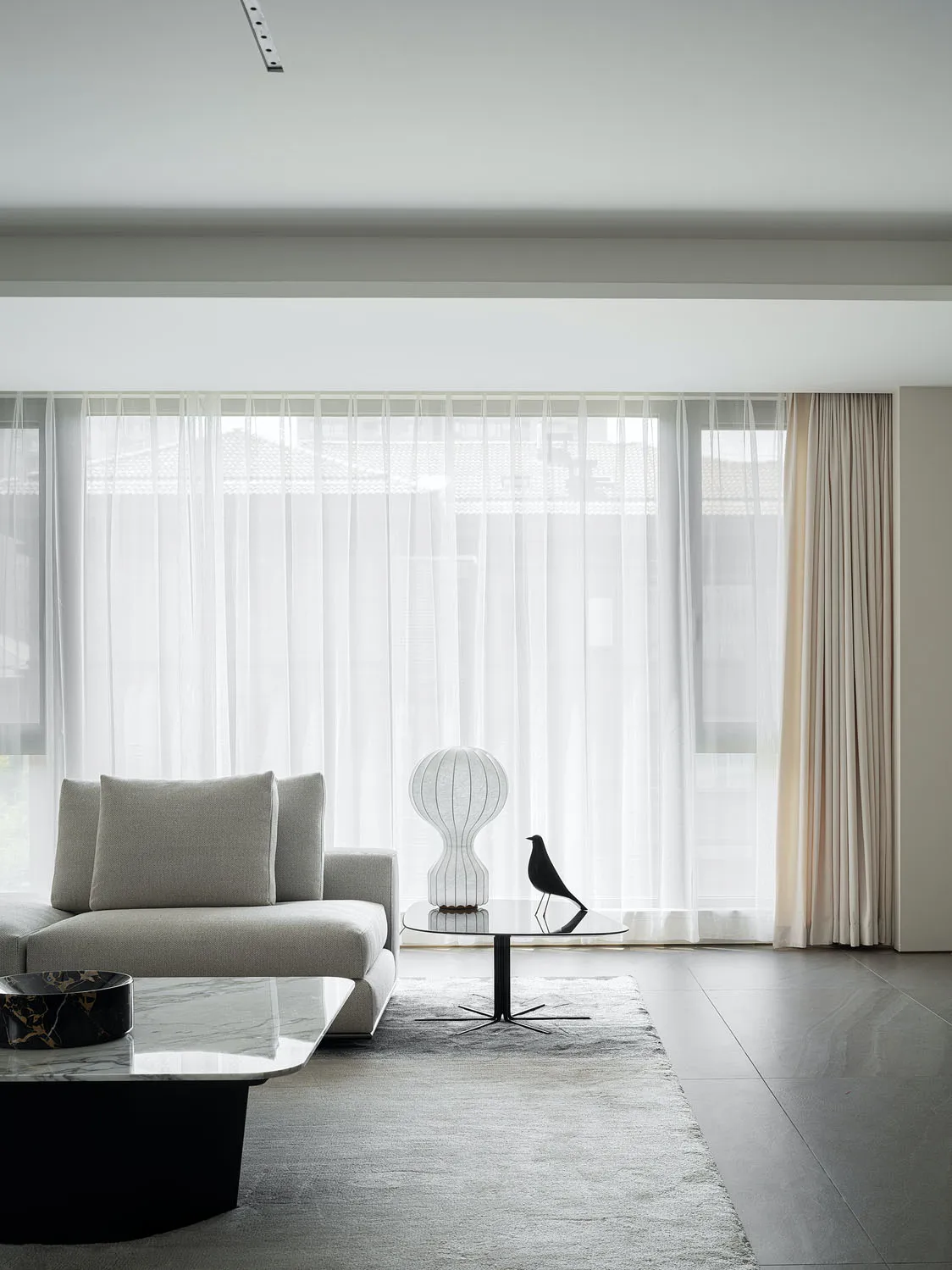 Modern living room featuring a glass coffee table, a stone floor, and white sheer curtains.