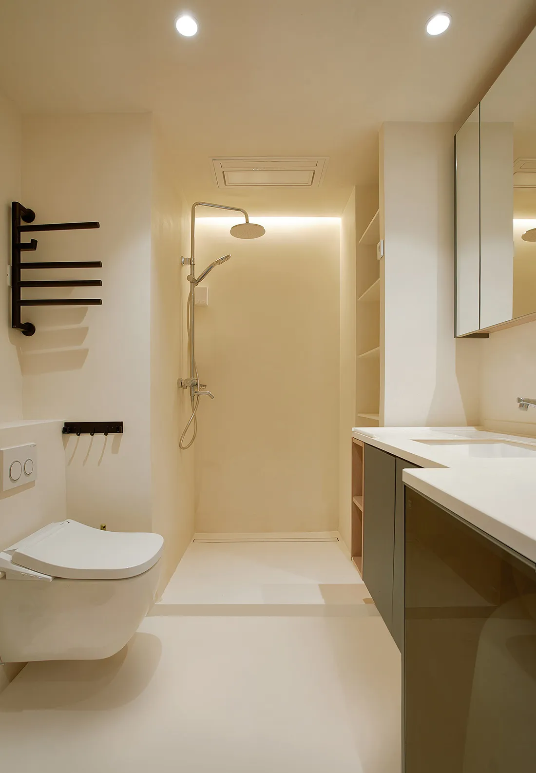 A minimalist bathroom with white tiled flooring and walls, featuring a toilet, a walk-in shower, and a sleek sink counter wit