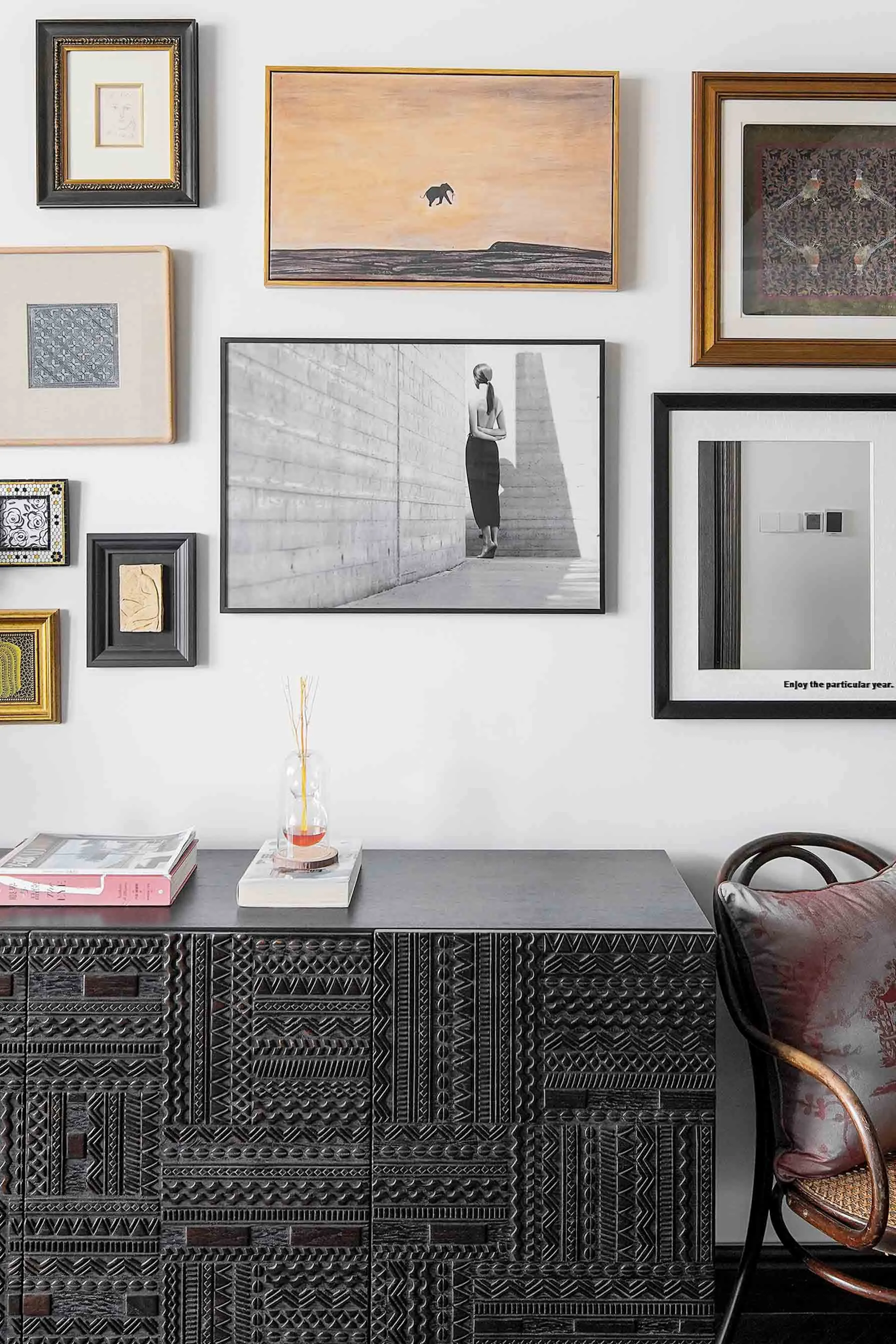 A wall adorned with various framed artworks, including a black-and-white photo of a woman and a painting of an elephant.