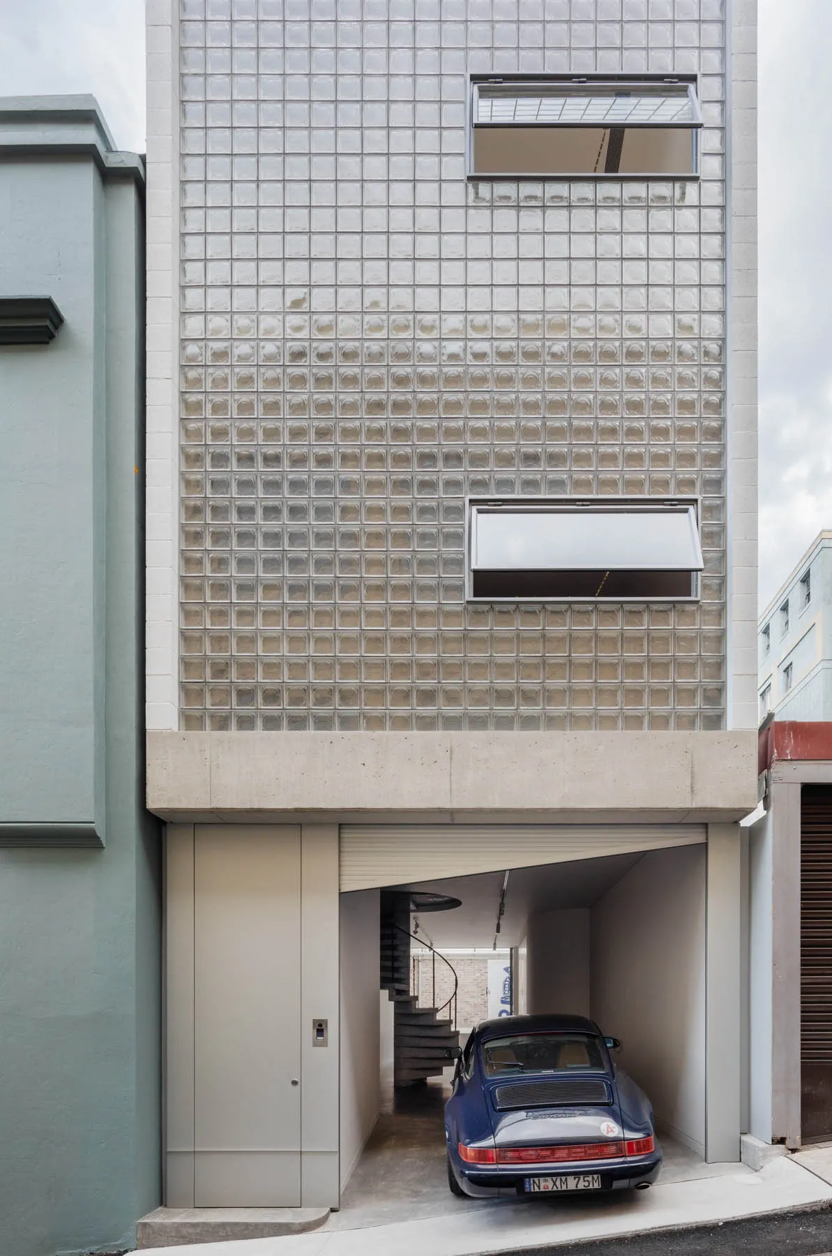 Modern building exterior featuring glass blocks and a blue sports car parked in the garage.