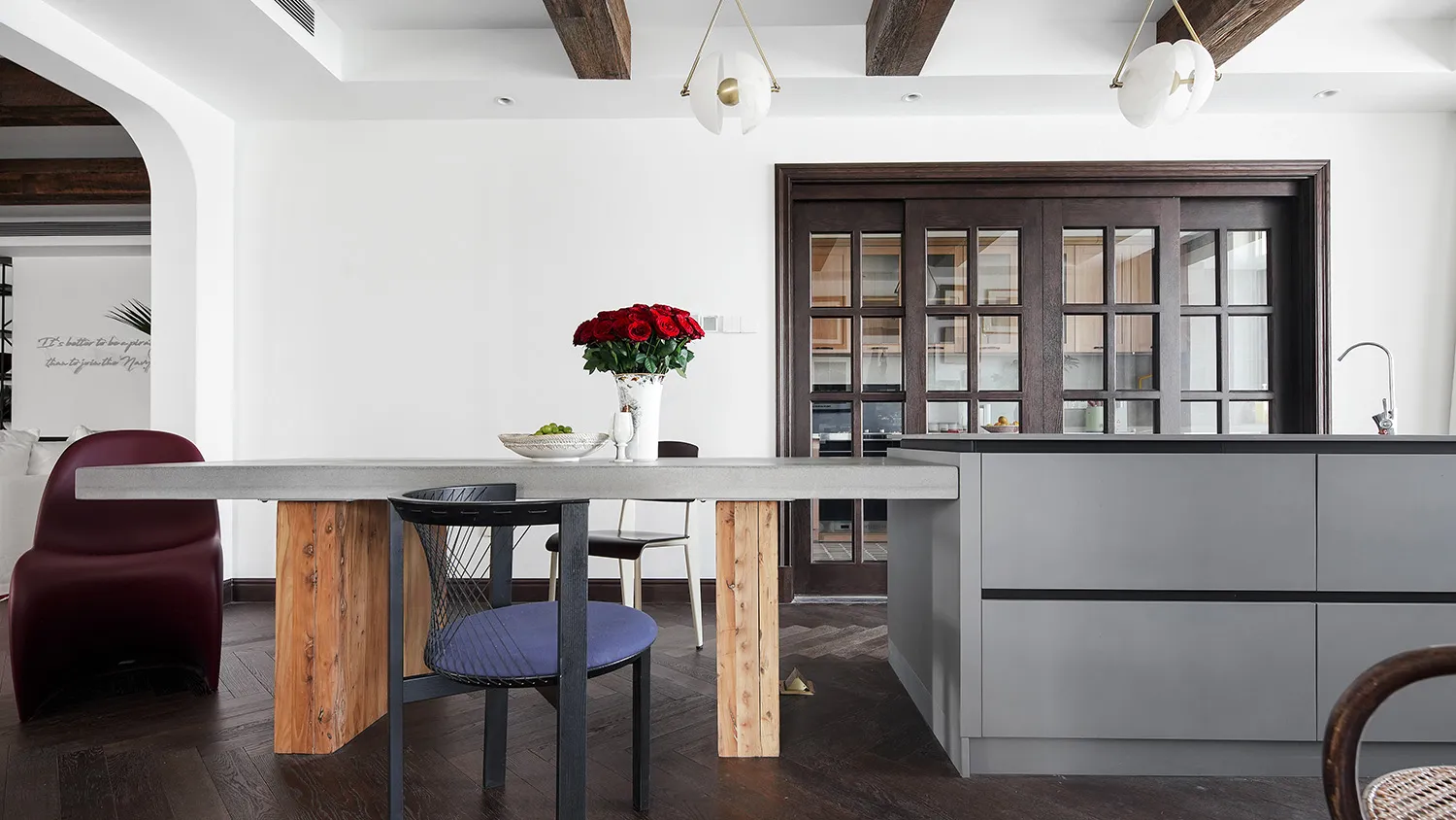 A modern kitchen featuring concrete countertops and wooden baseboards with a vase of red roses on the table.