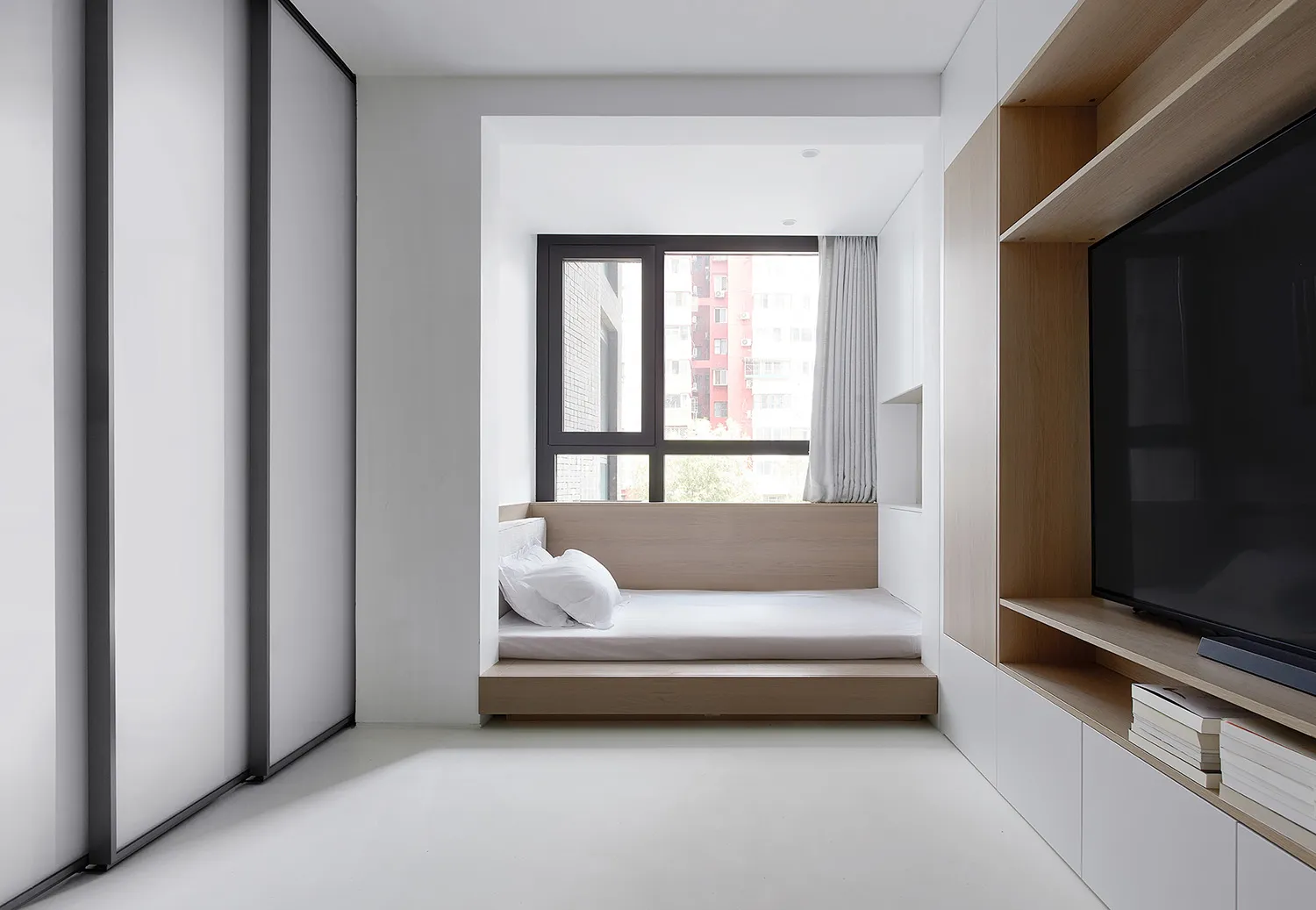 A minimalist bedroom with a bed platform, window, and built-in shelves.