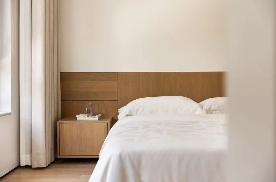 A minimalist bedroom with a wooden headboard and white bedding.