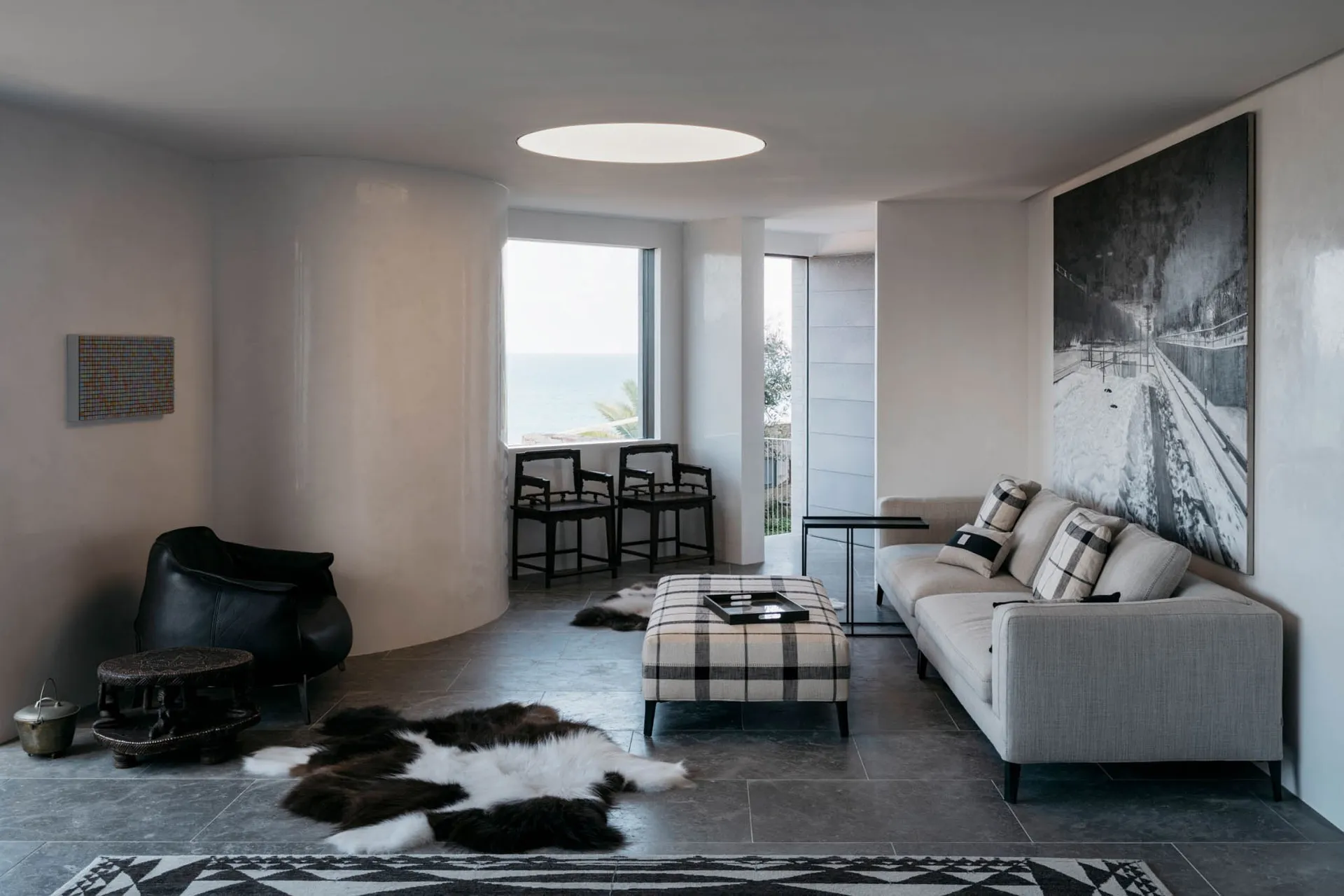 A modern living room featuring a minimalist interior design with concrete walls and floor, a large sofa, and large windows wi