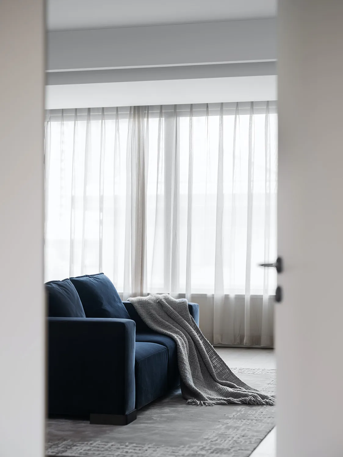 A minimalist living room with a blue sofa, gray throw blanket, and textured cushions.