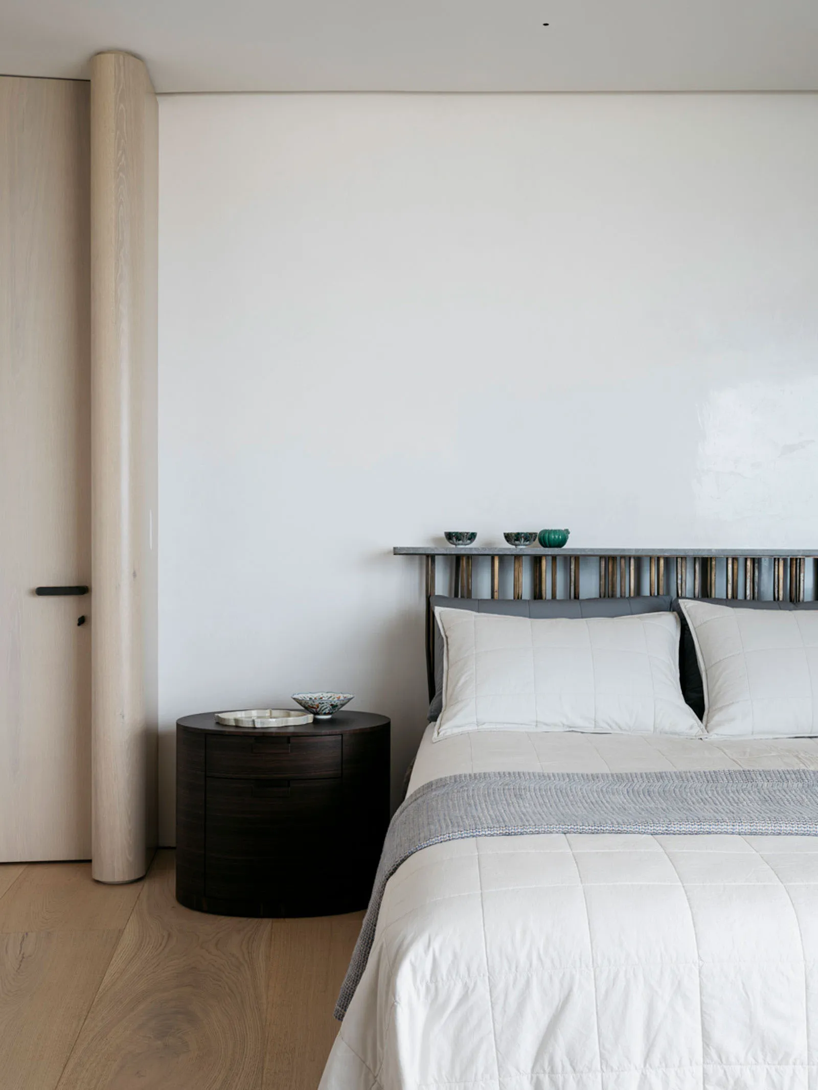 A minimalist bedroom featuring a bed with a wooden headboard, a metal shelf, and fabric bedding.