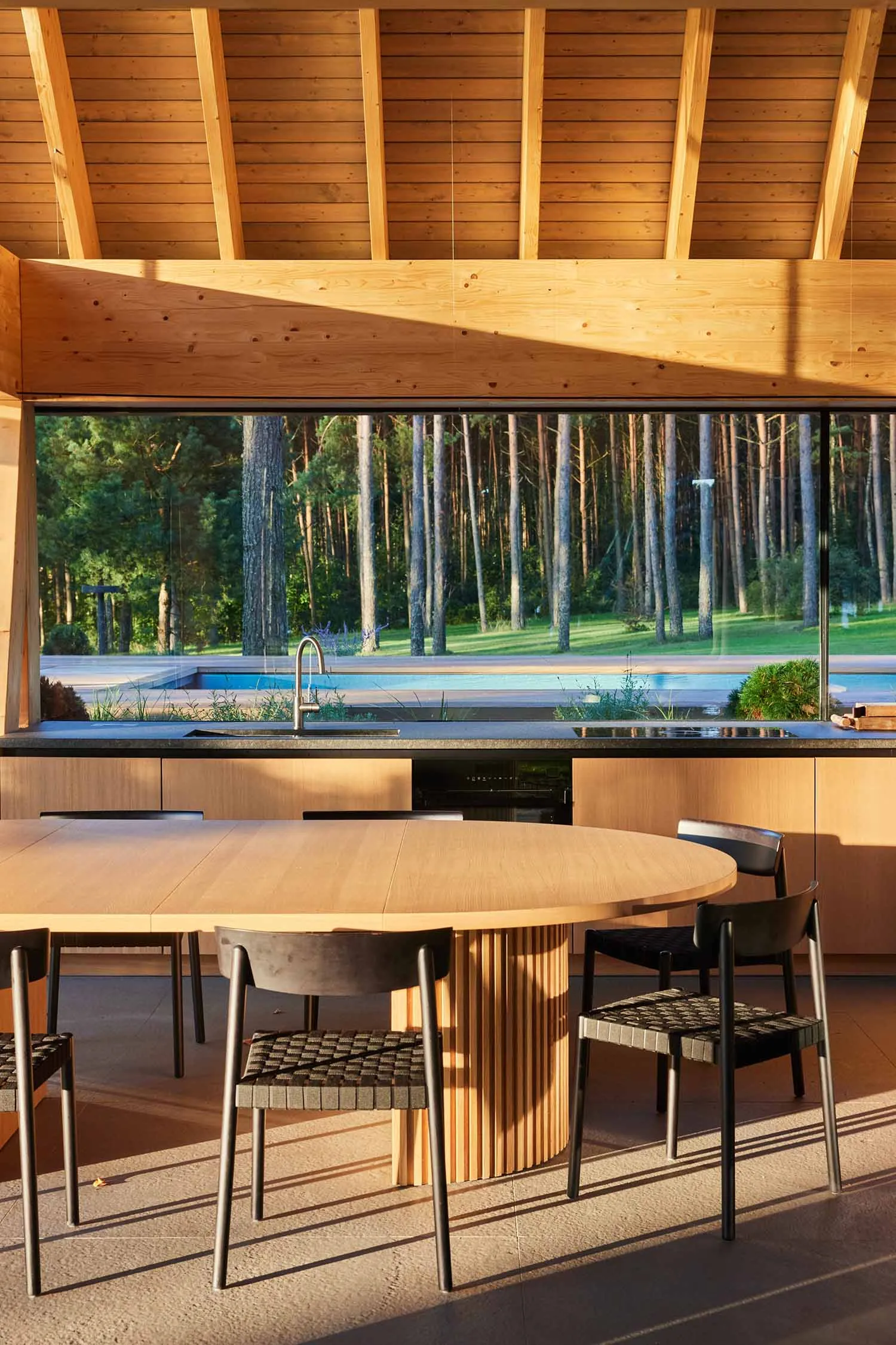 A modern minimalist kitchen with wooden elements and a view of a forest through the large window.