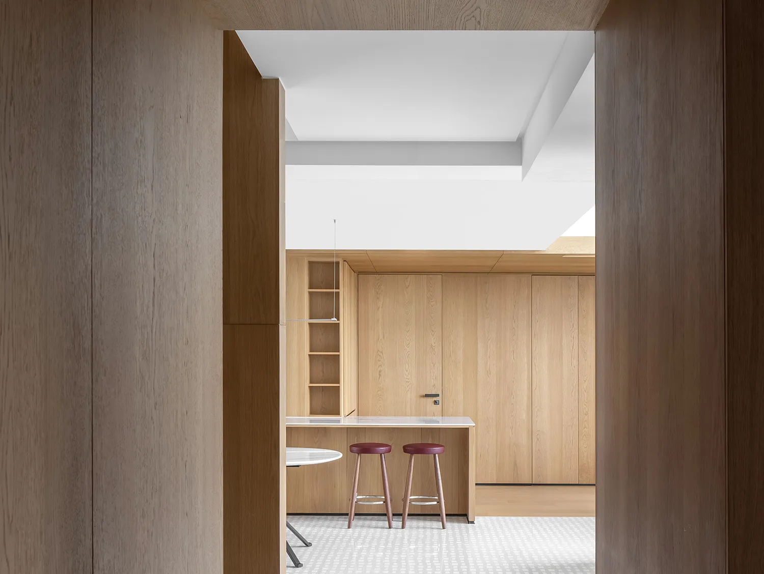A modern minimalist kitchen with wooden cabinets and stools, featuring a clean and functional design.