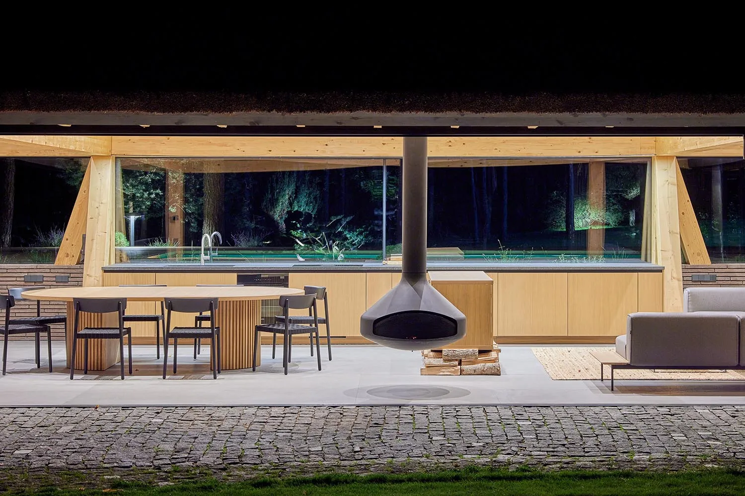 A modern outdoor kitchen with wooden elements and a hanging fireplace.