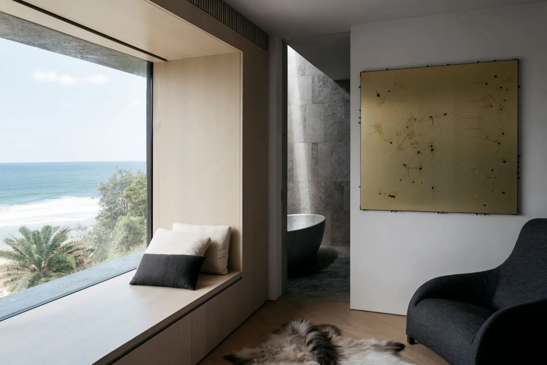 A modern residential interior featuring a window with a view of the ocean, a seating area with cushions, a large artwork, and