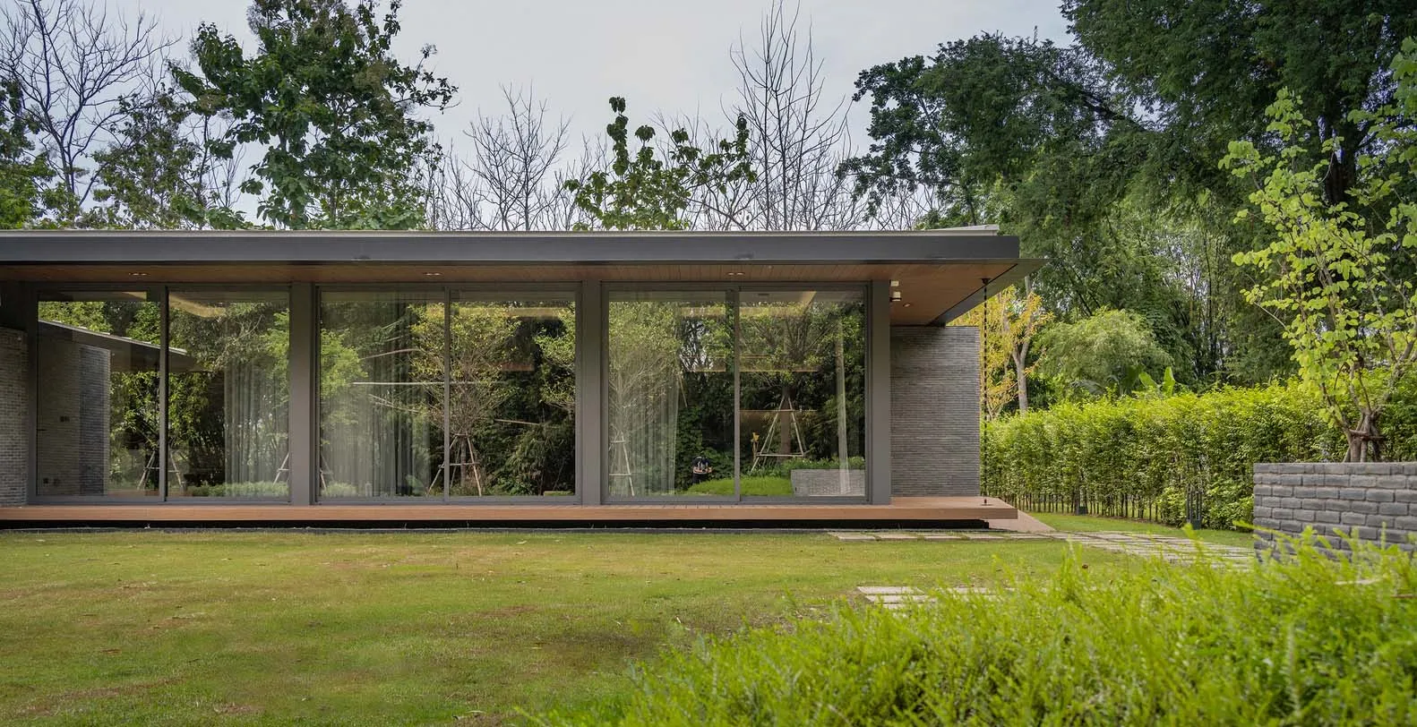 A modern house with large glass windows and a flat roof, surrounded by greenery.