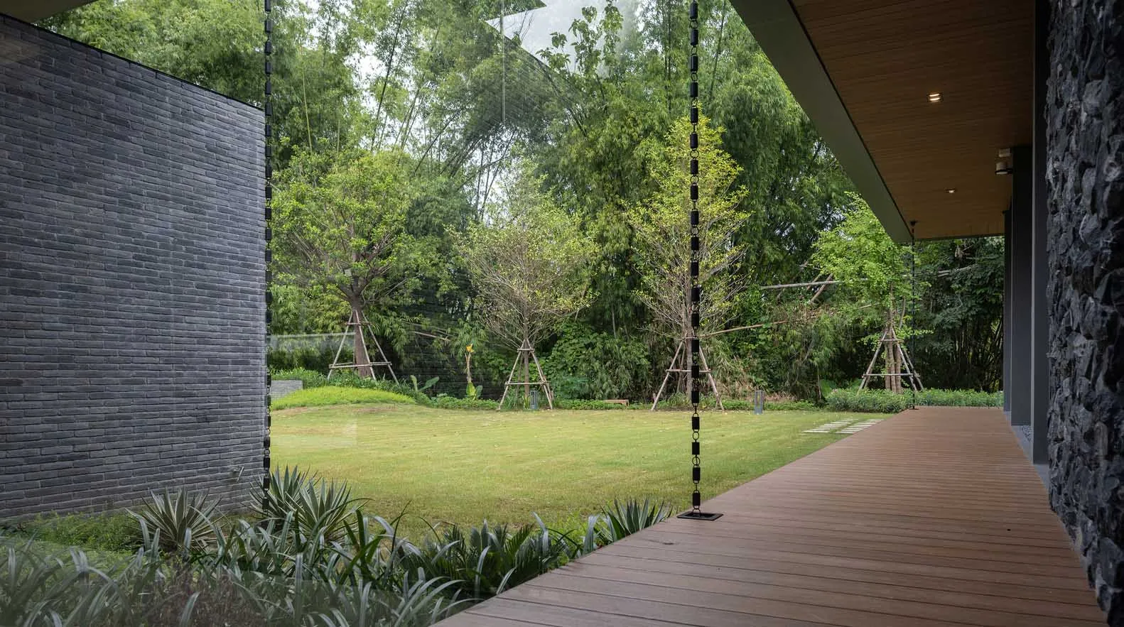 Modern outdoor space featuring a wooden deck, stone walls, and glass elements surrounded by lush greenery.
