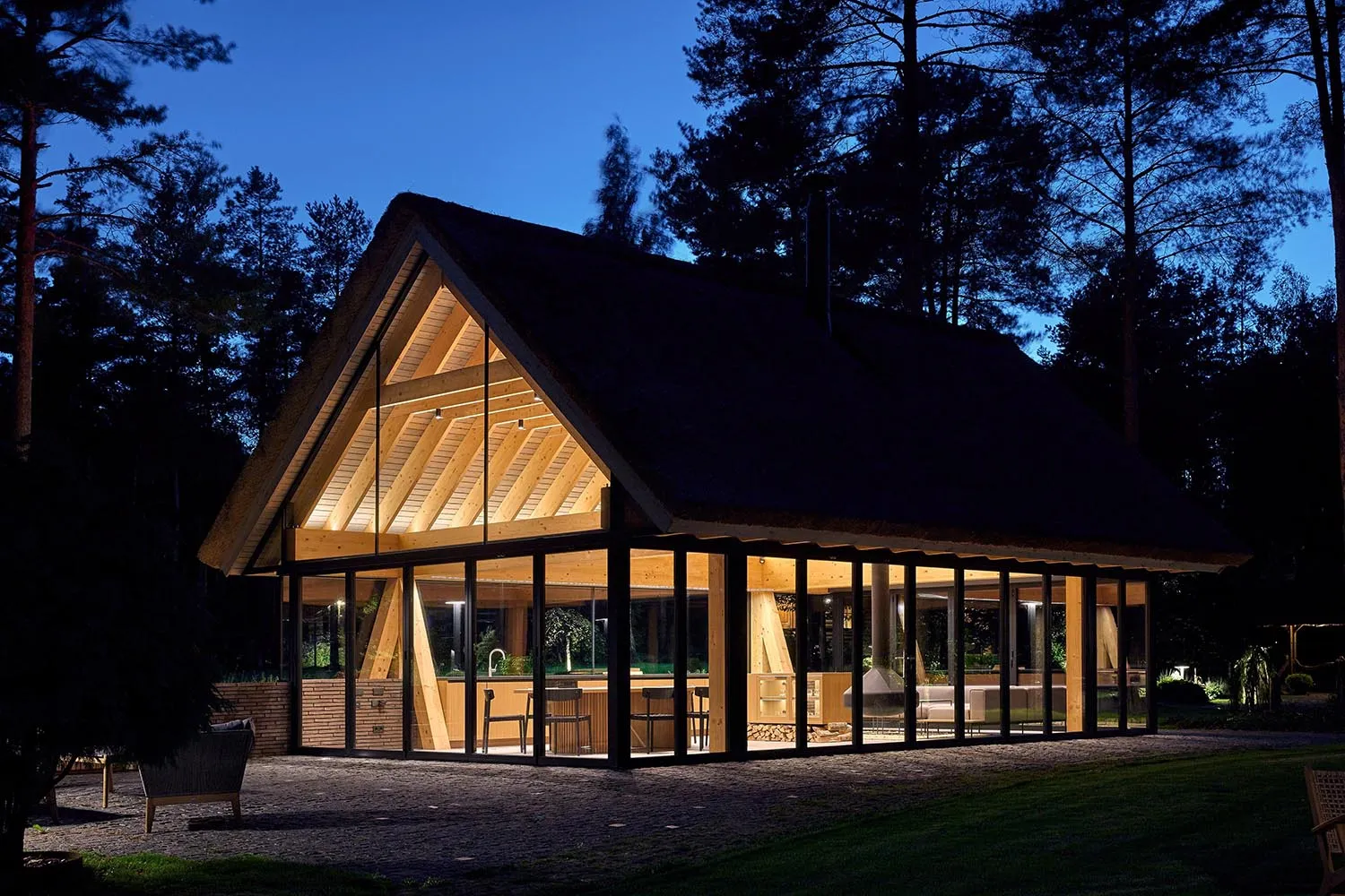 A modern residential building illuminated at night, featuring large glass windows and wooden structural elements.
