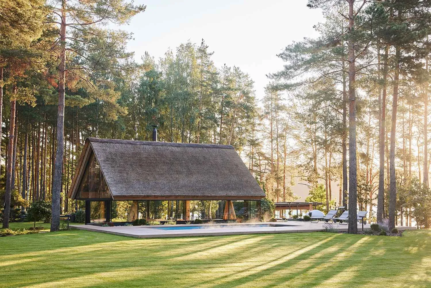 Modern rural house with wooden shingles surrounded by trees and a grassy lawn.