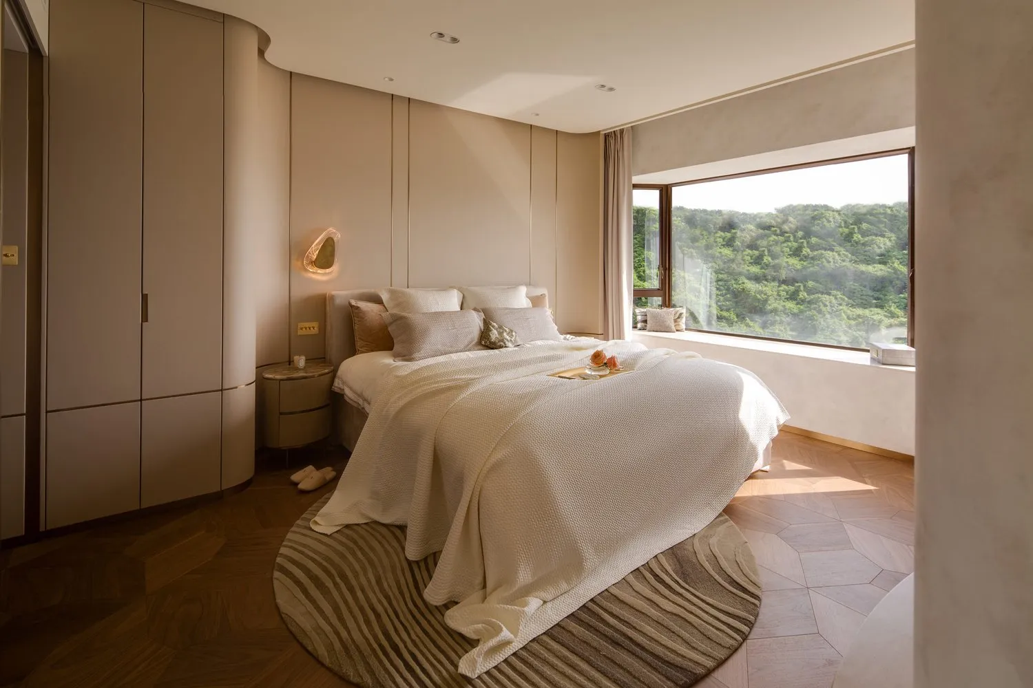 A modern bedroom with white cushions on the bed, a large window with a view of greenery, and a minimalist design.