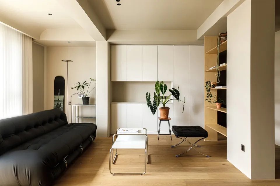 Modern minimalist living room with a black leather sofa, wooden flooring, and white cabinets.