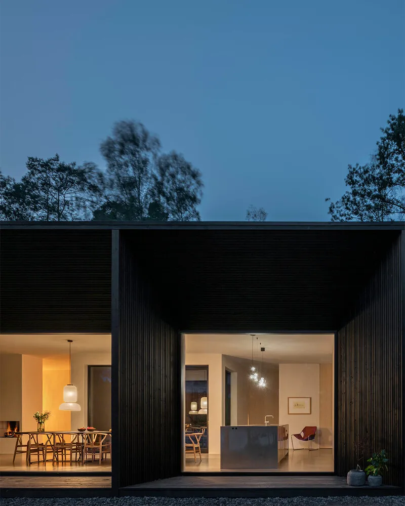 A modern house exterior with wooden panels and large windows at dusk.