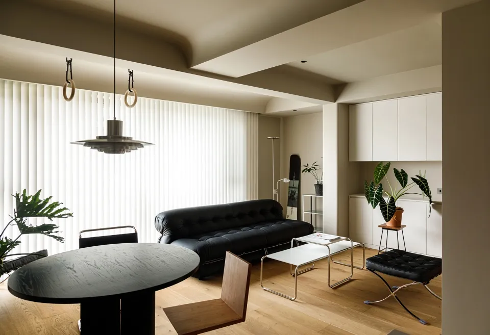 A modern living room with a black sofa, white blinds, and minimalist decor.