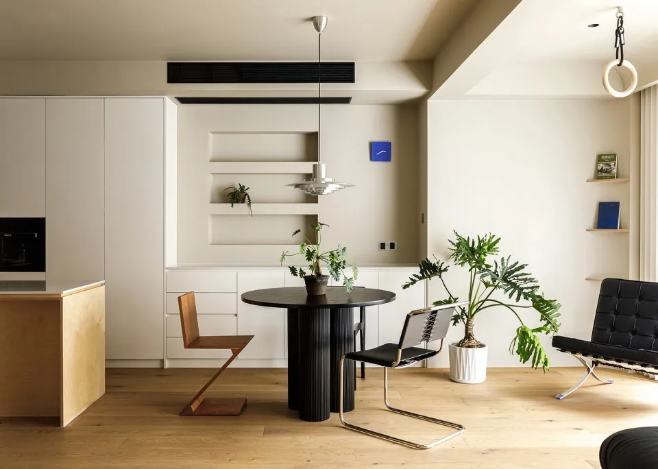 A modern residential kitchen with hardwood flooring, featuring sleek black appliances and a round dining table with green pla